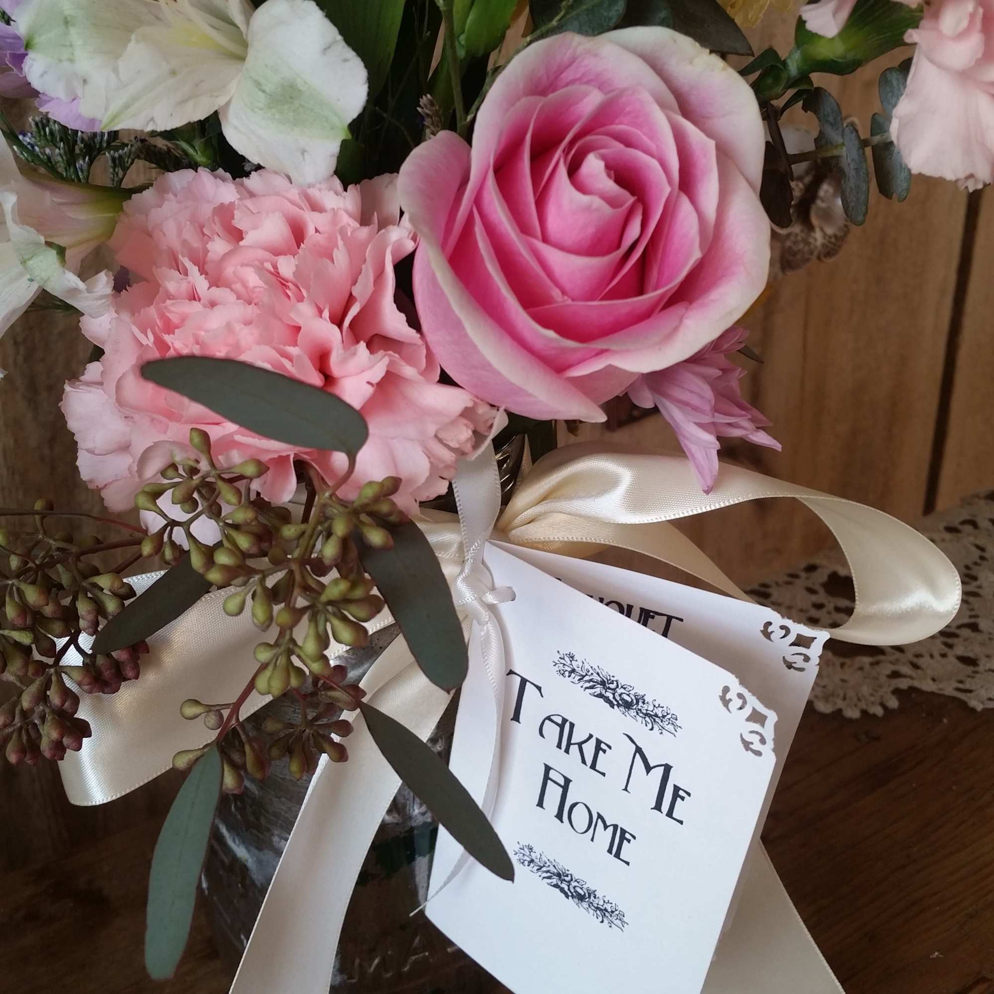 Pink rose and carnations in a glass vase with a ribbon and gift tag