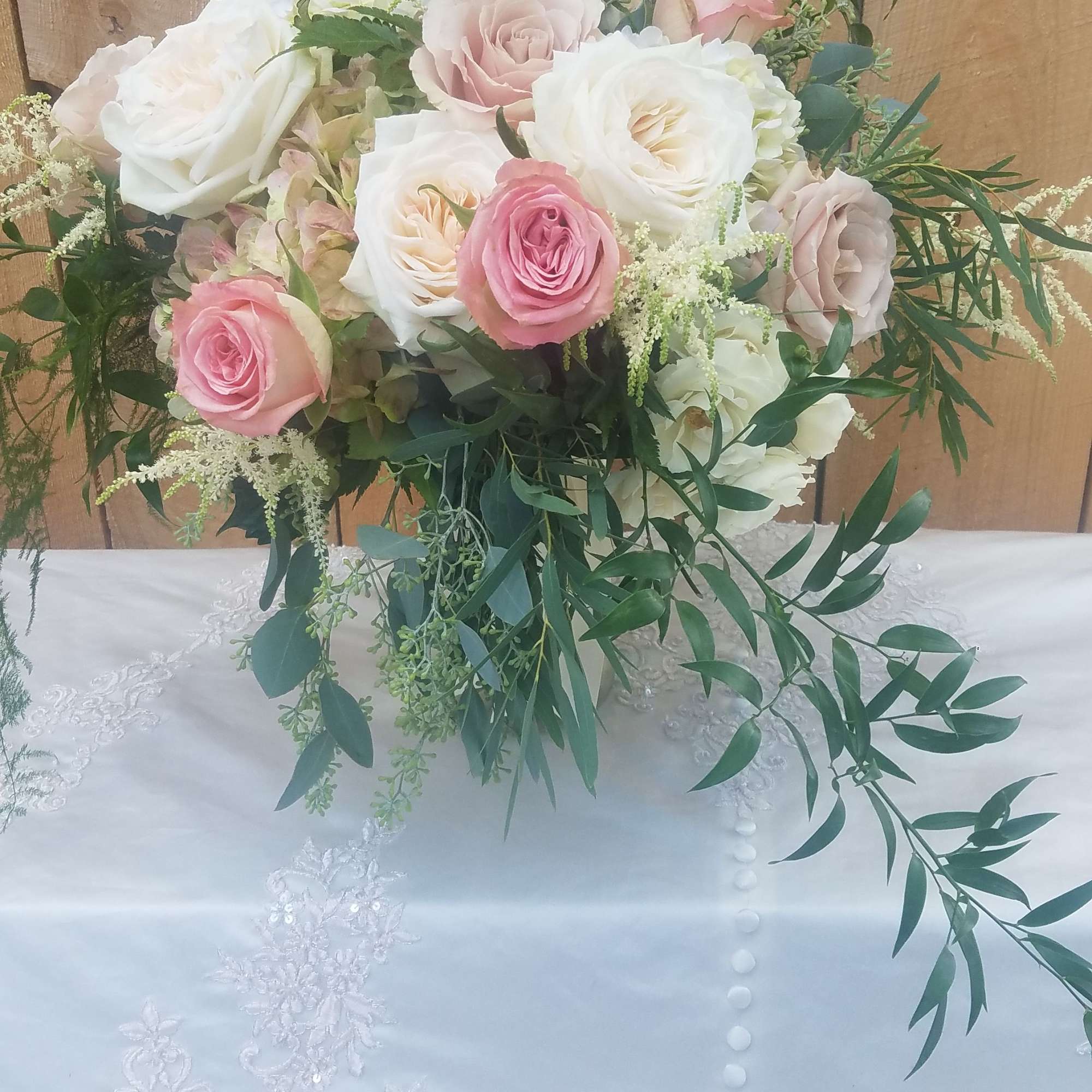 Pink and white rose bouquet with trailing greenery on a lace-covered table