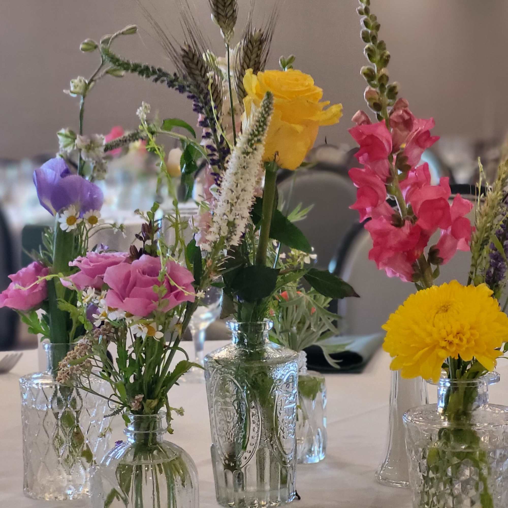Small mixed flower arrangements in clear glass bottles on a table