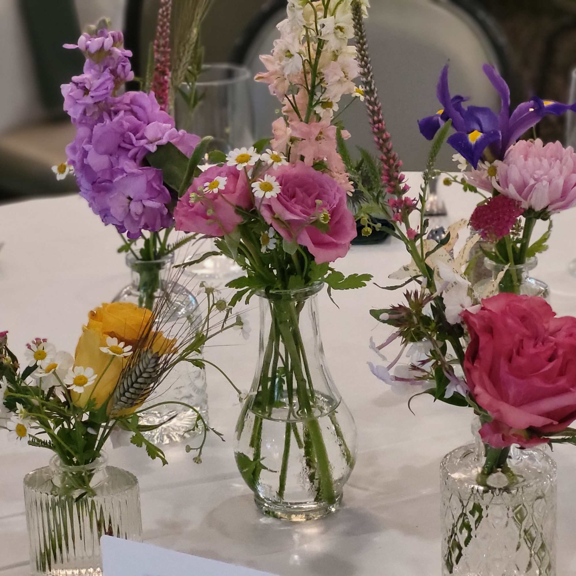 Small mixed flower arrangements in clear glass vases on a table, photo 3 of 8