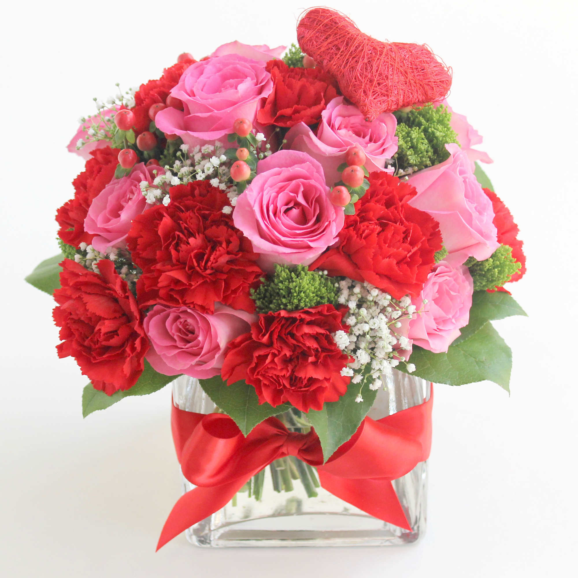 Pink roses and red carnations in a glass vase with a red ribbon