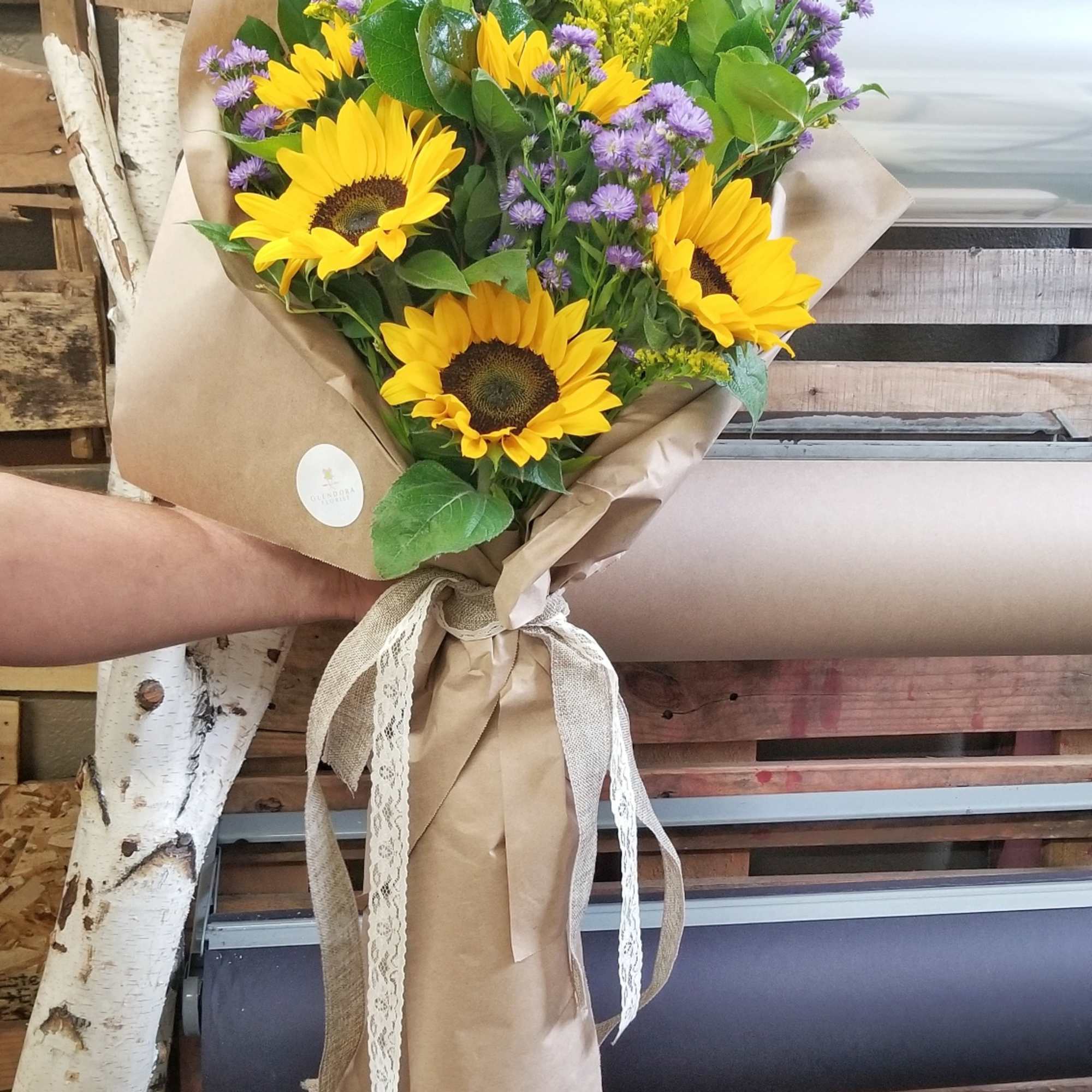 Bouquet of sunflowers and purple filler flowers wrapped in brown paper