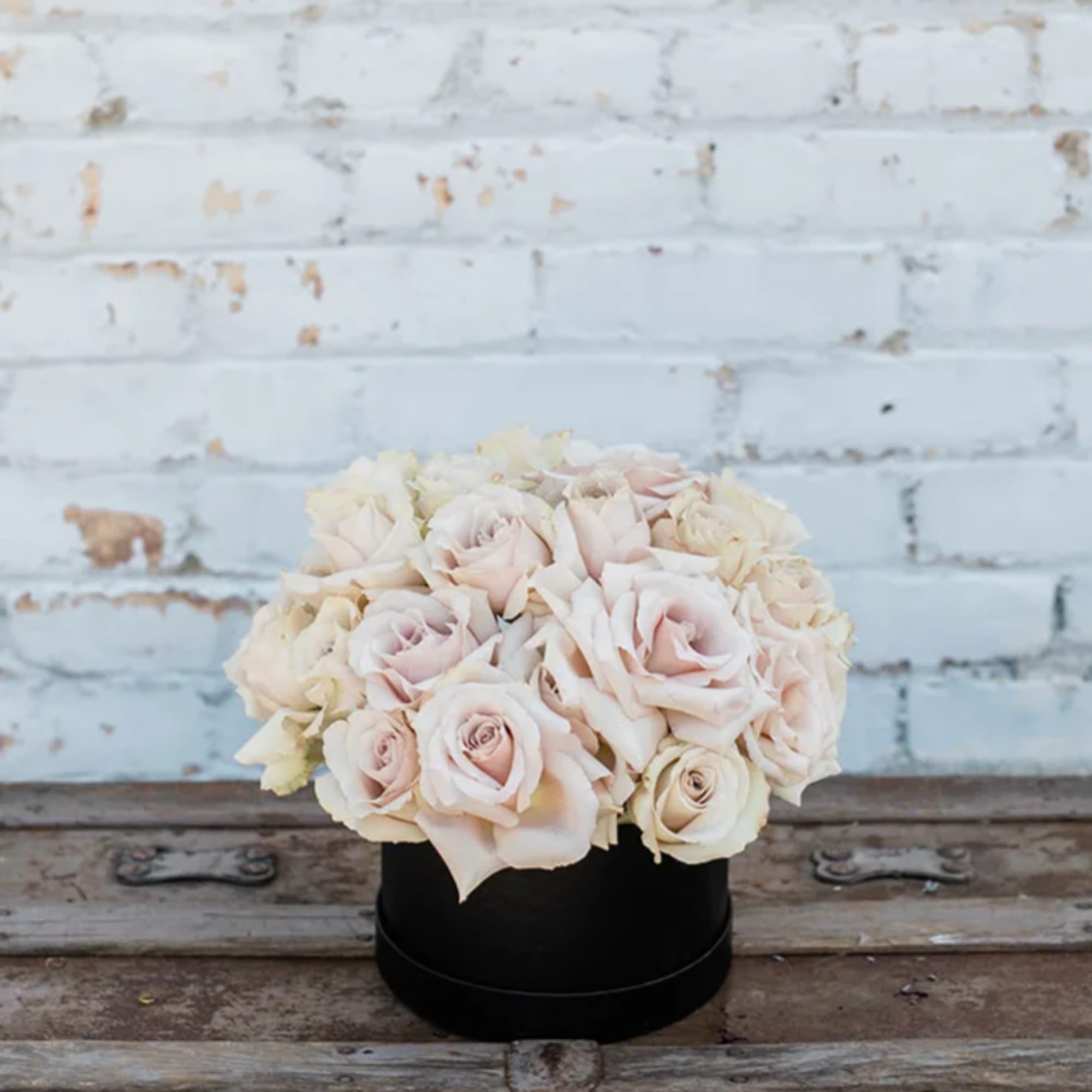Blush and cream roses arranged in a black round box