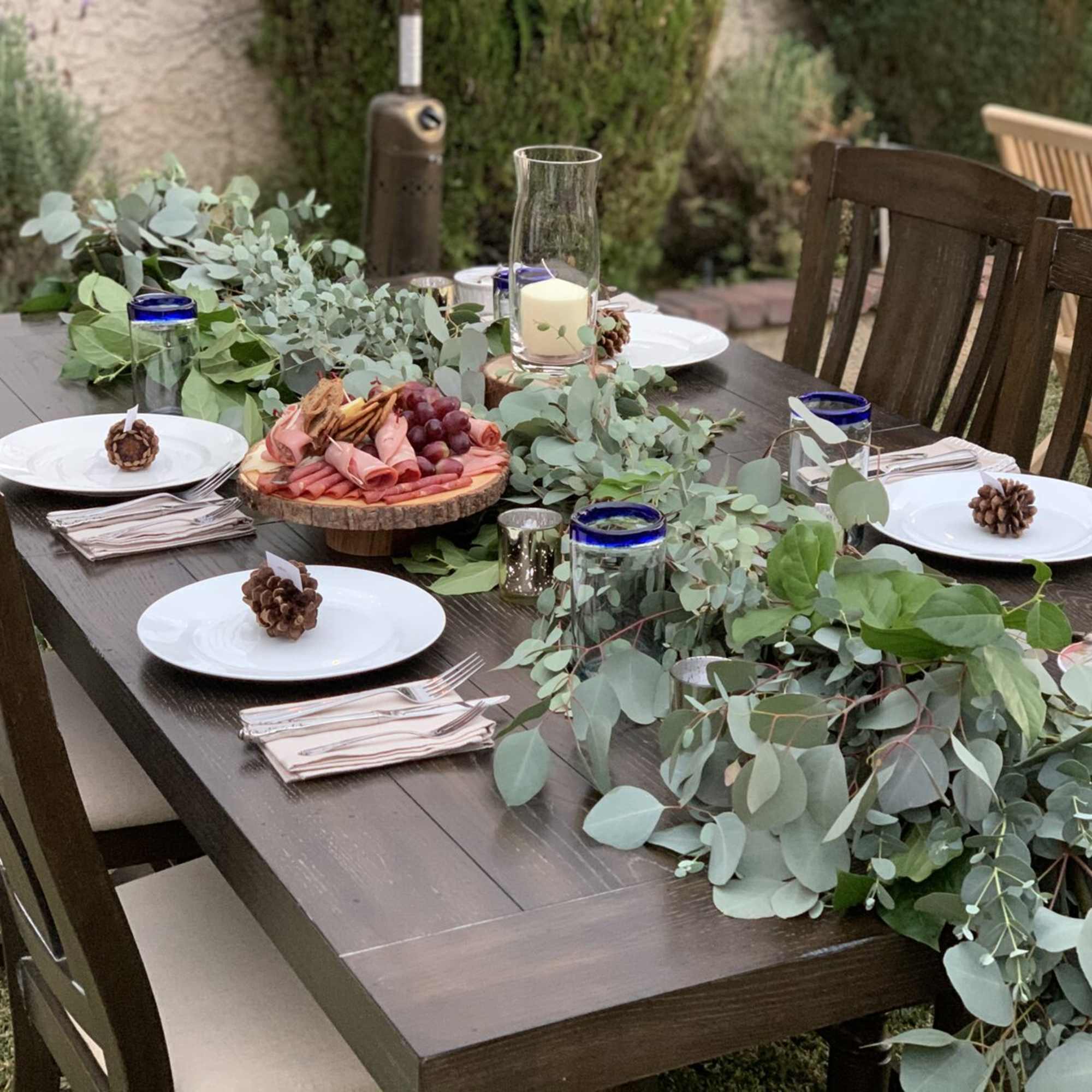 Outdoor dining table with eucalyptus garland, plates, candles, and a charcuterie board