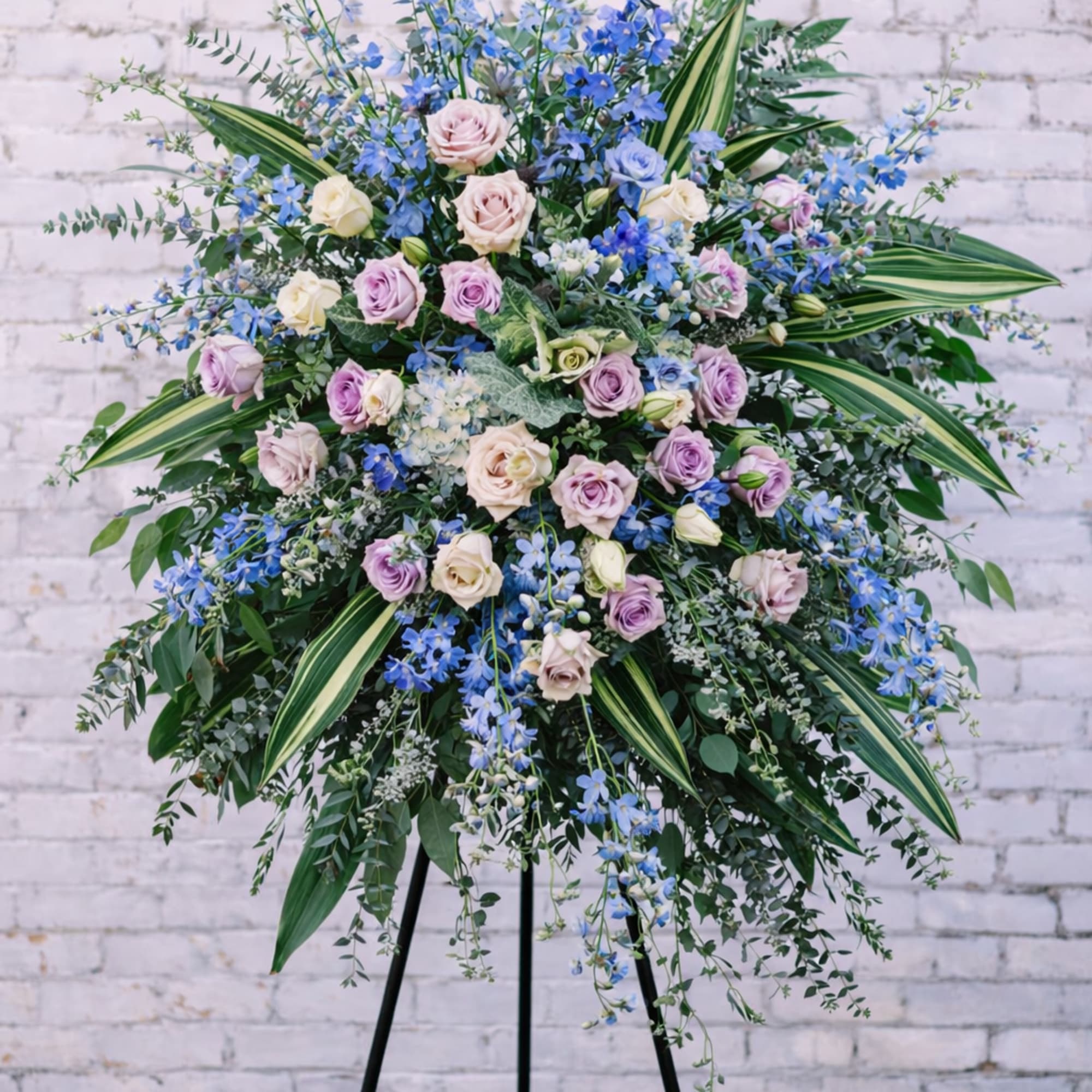 Large standing floral spray with pastel roses and blue flowers on a black easel