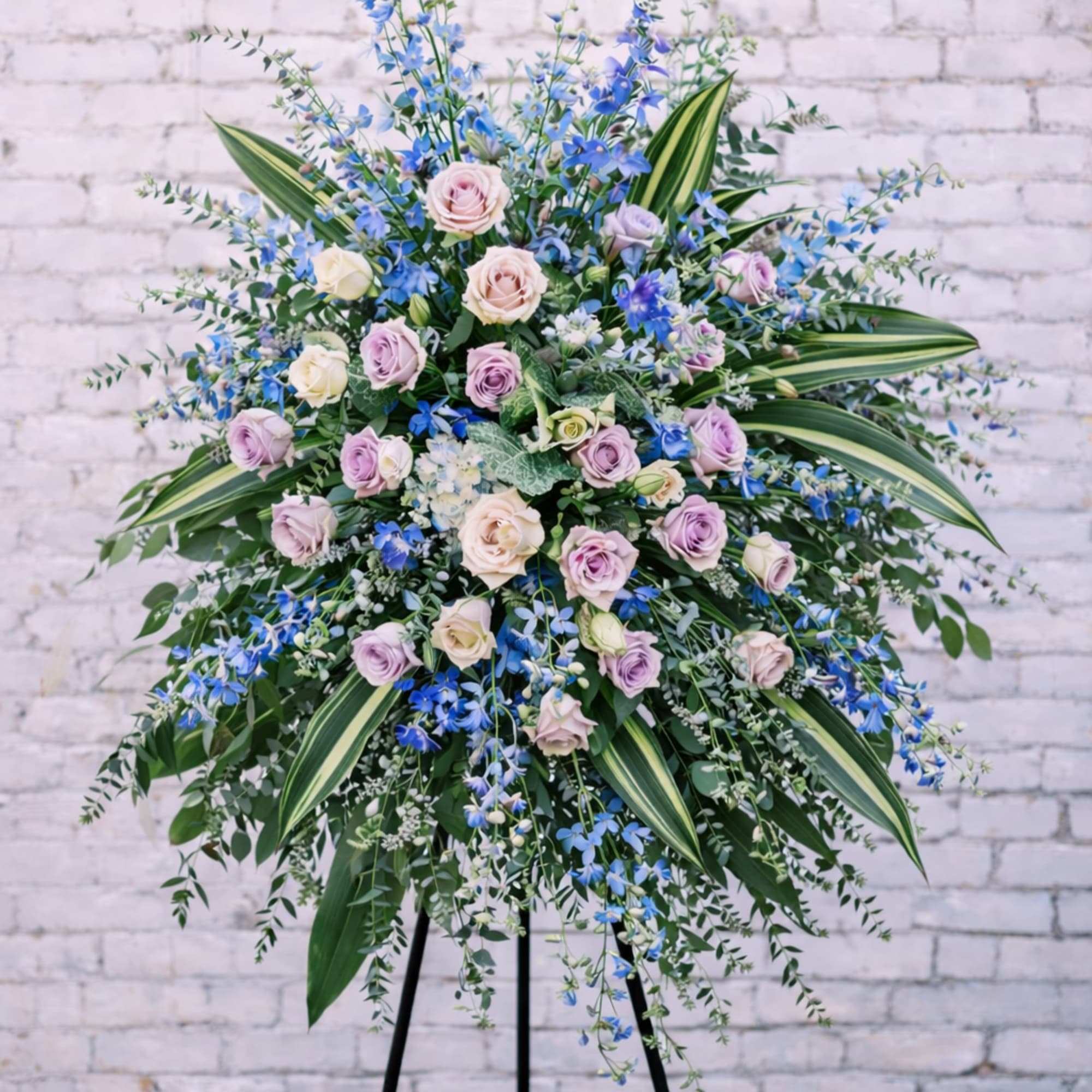 Large standing floral spray with pastel roses and blue flowers on a black easel