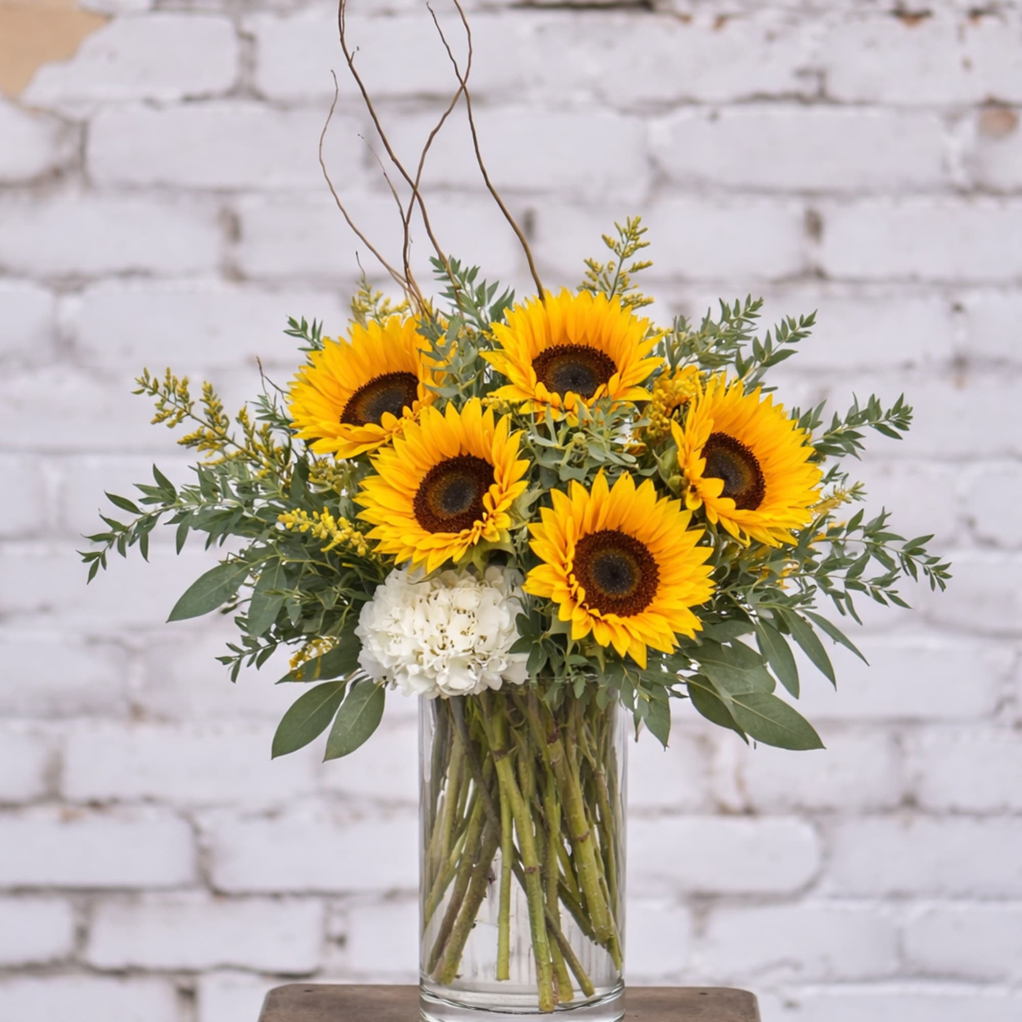 Sunflower arrangement in a clear glass vase with white accent blooms