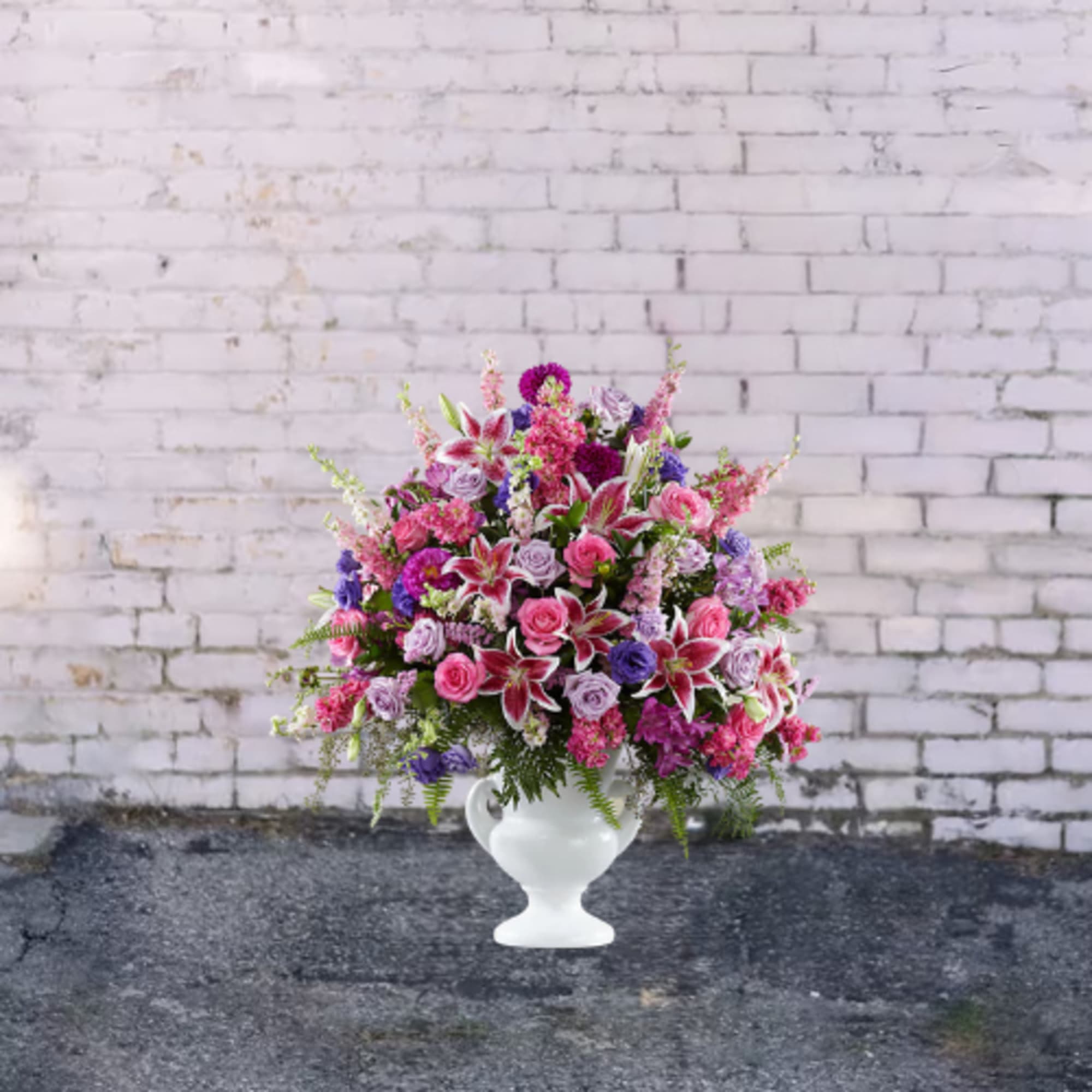 Pink and purple floral arrangement in a white urn vase