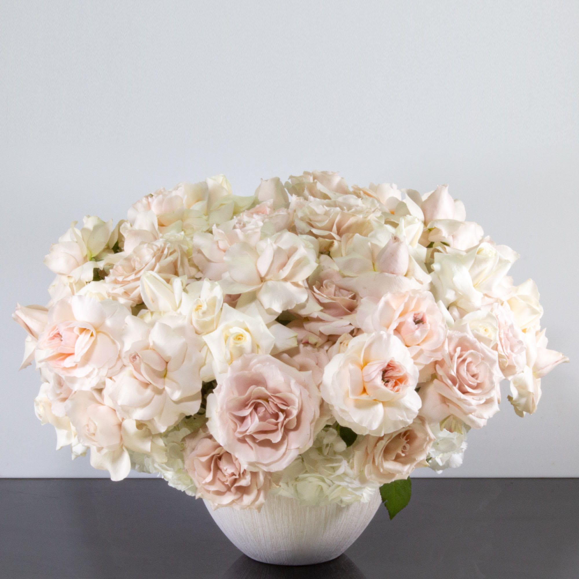 Low arrangement of blush and ivory roses in a white bowl-shaped vase