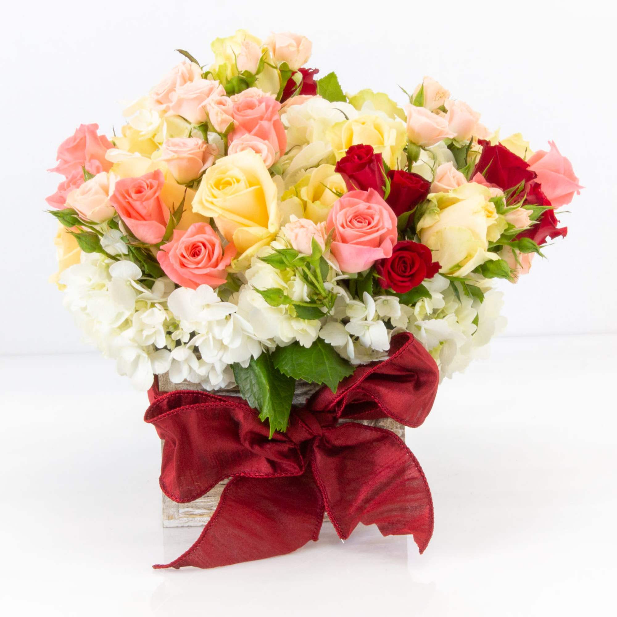 Mixed roses in a white container with a red ribbon