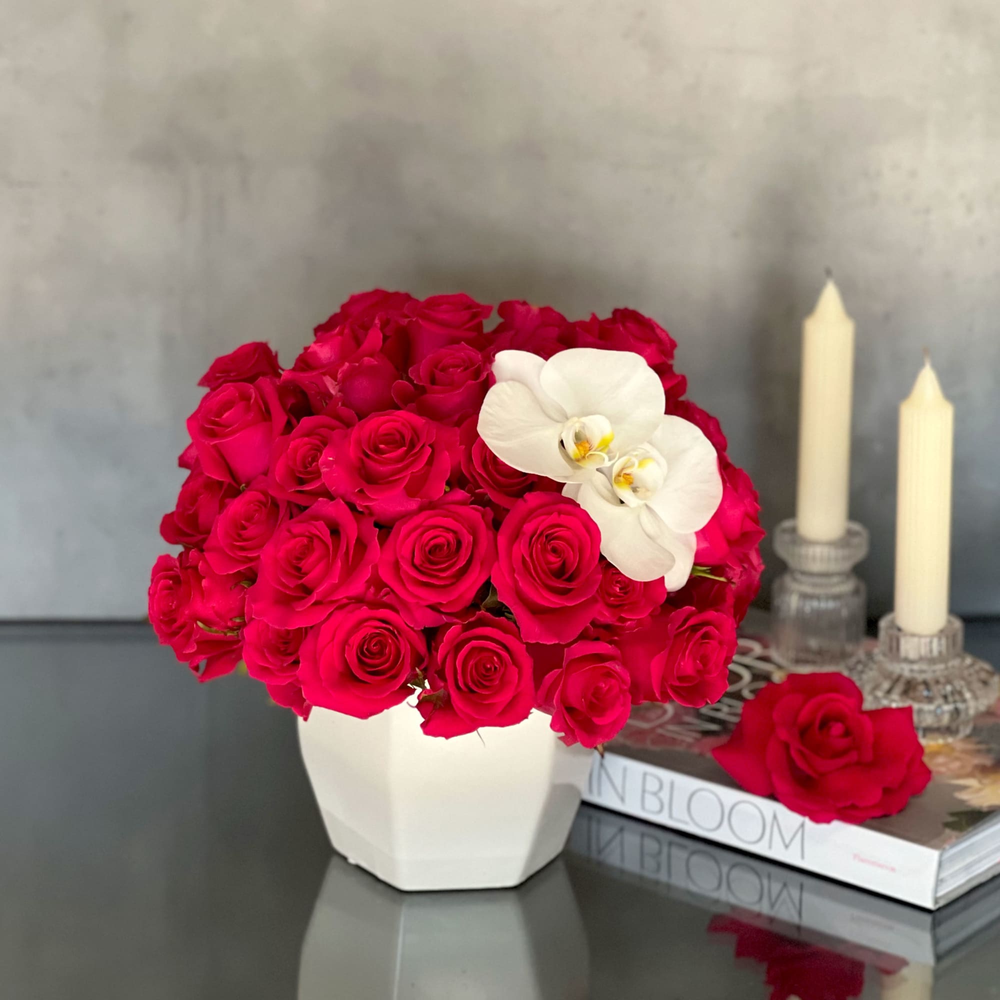 Hot pink rose arrangement in a white vase with a white orchid accent