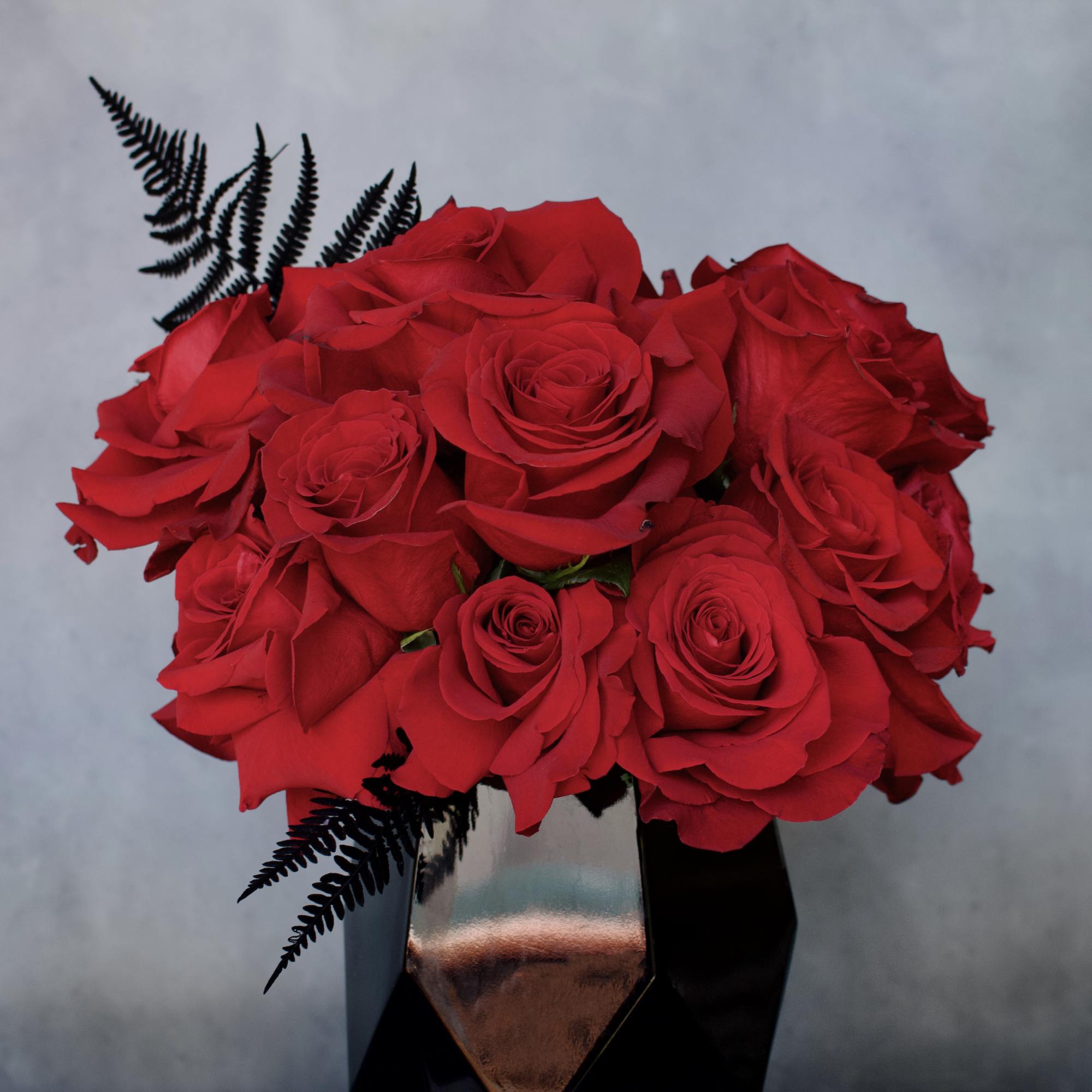Compact arrangement of red roses with black fern in a faceted black vase