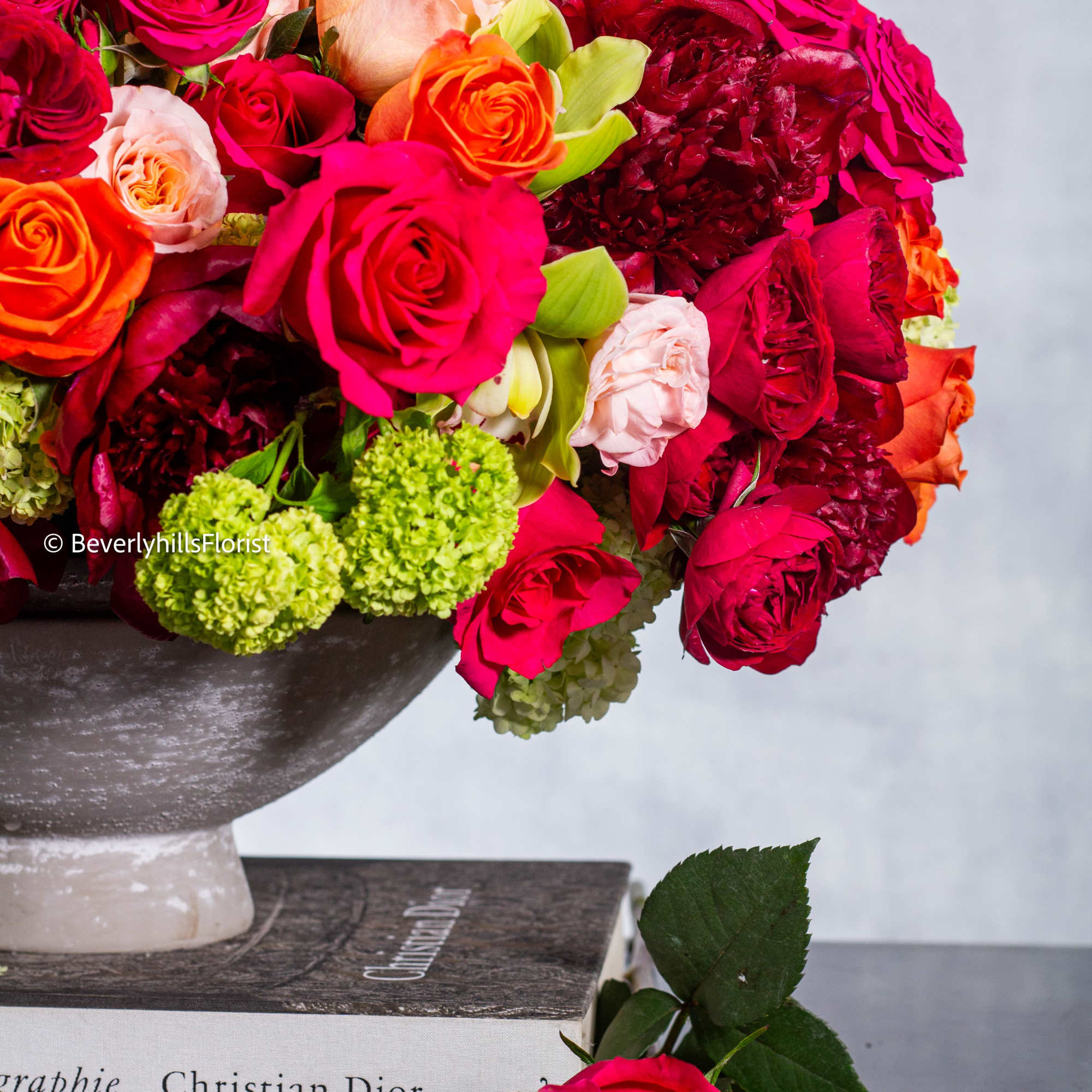 Bright mixed rose arrangement in a pedestal vase with a single rose on the table