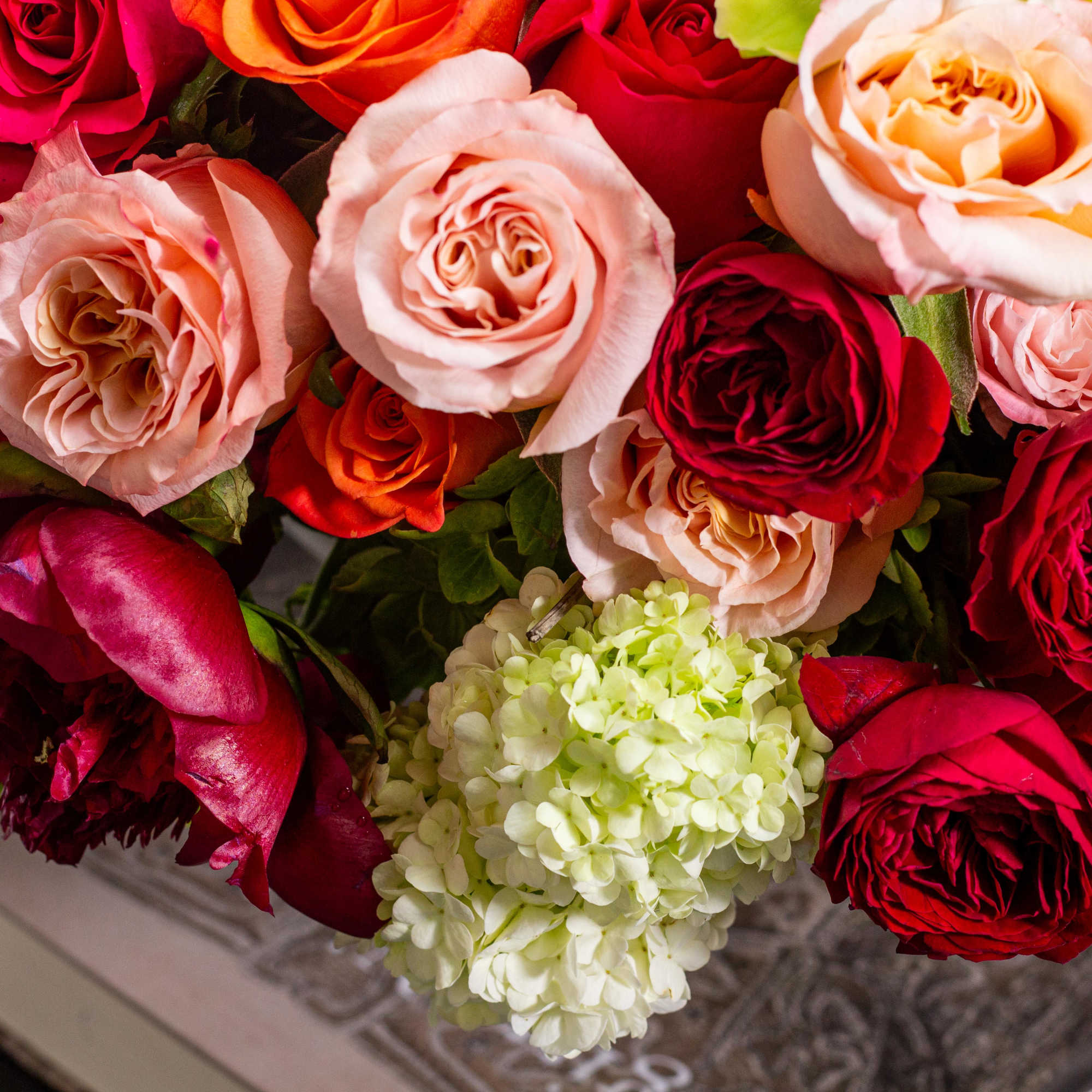 Close-up bouquet of red, pink, and peach roses with pale hydrangea.