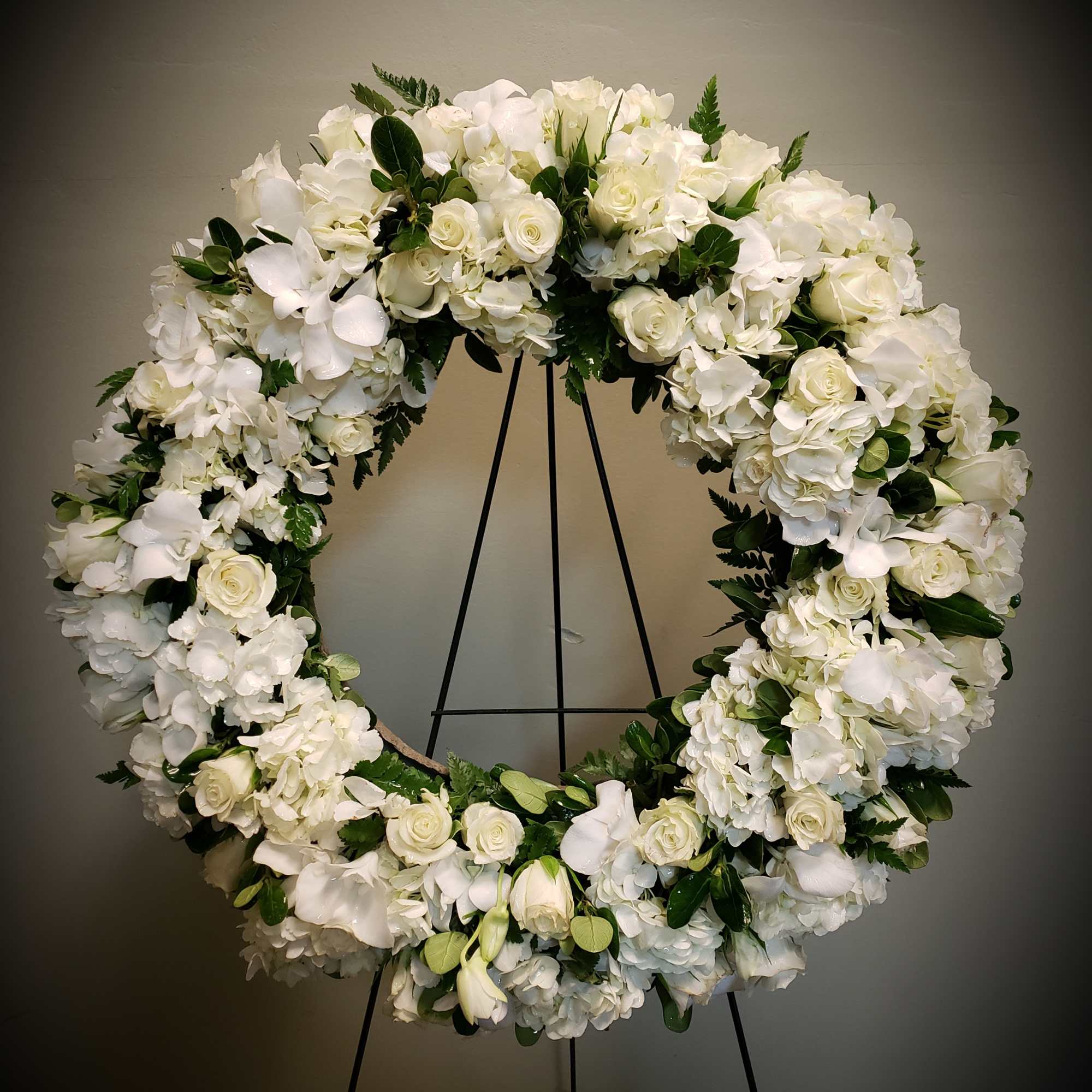 Large all-white floral wreath with roses and hydrangeas on a tall metal easel stand