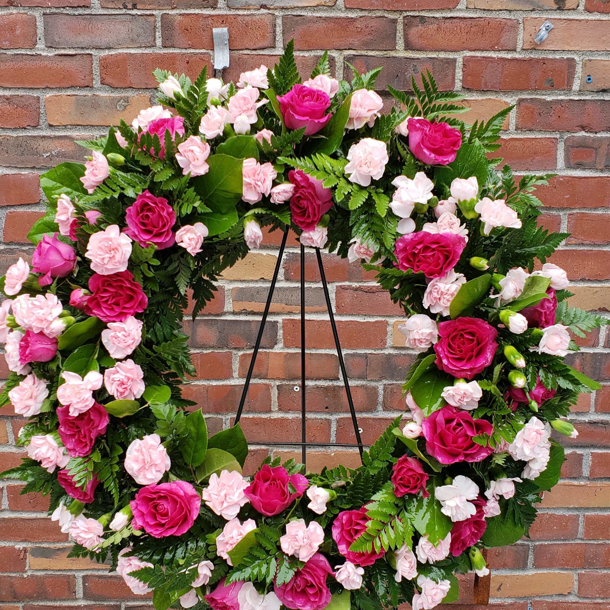 Standing wreath of hot pink roses and light pink carnations on a metal easel