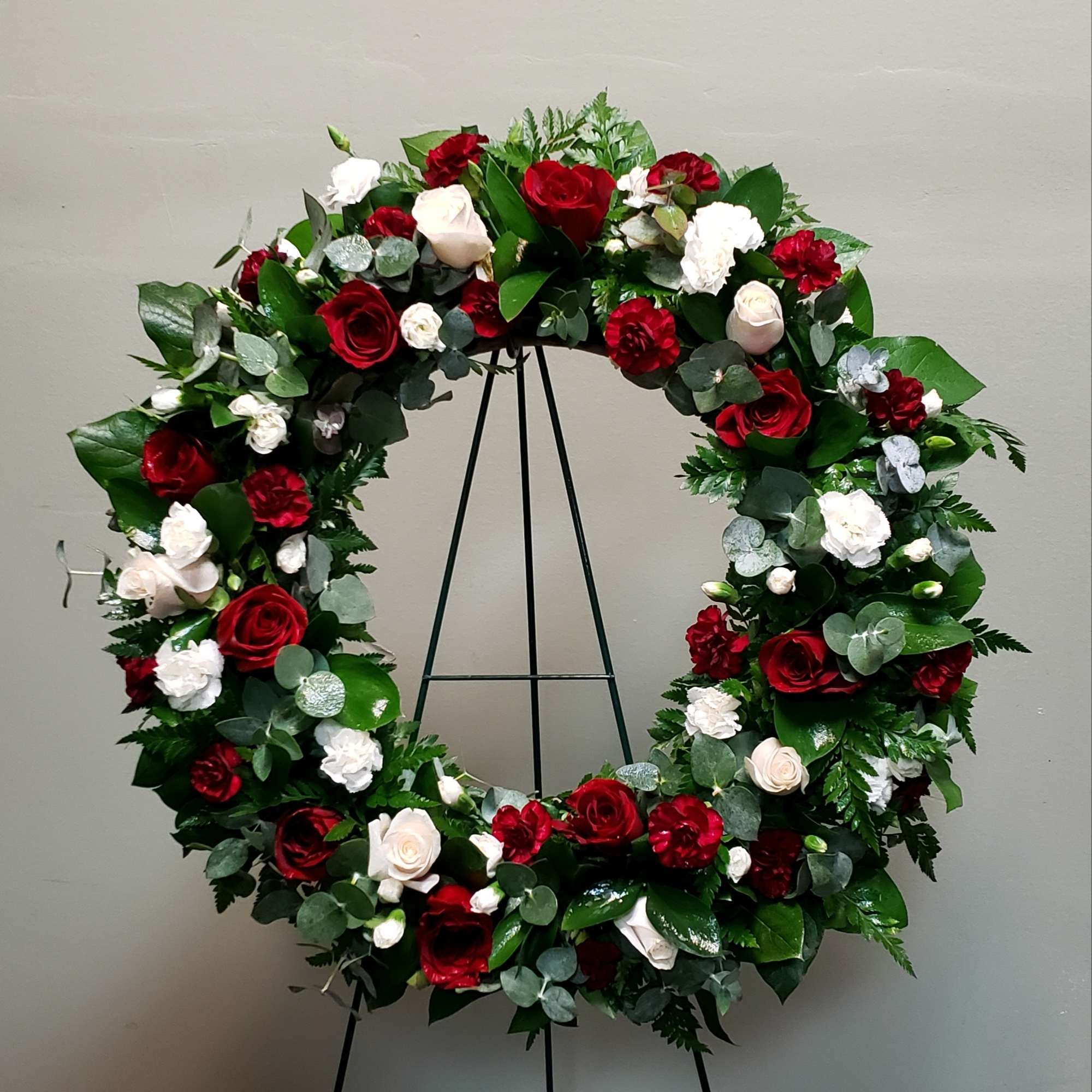 Standing wreath of red and white roses and carnations on a metal easel