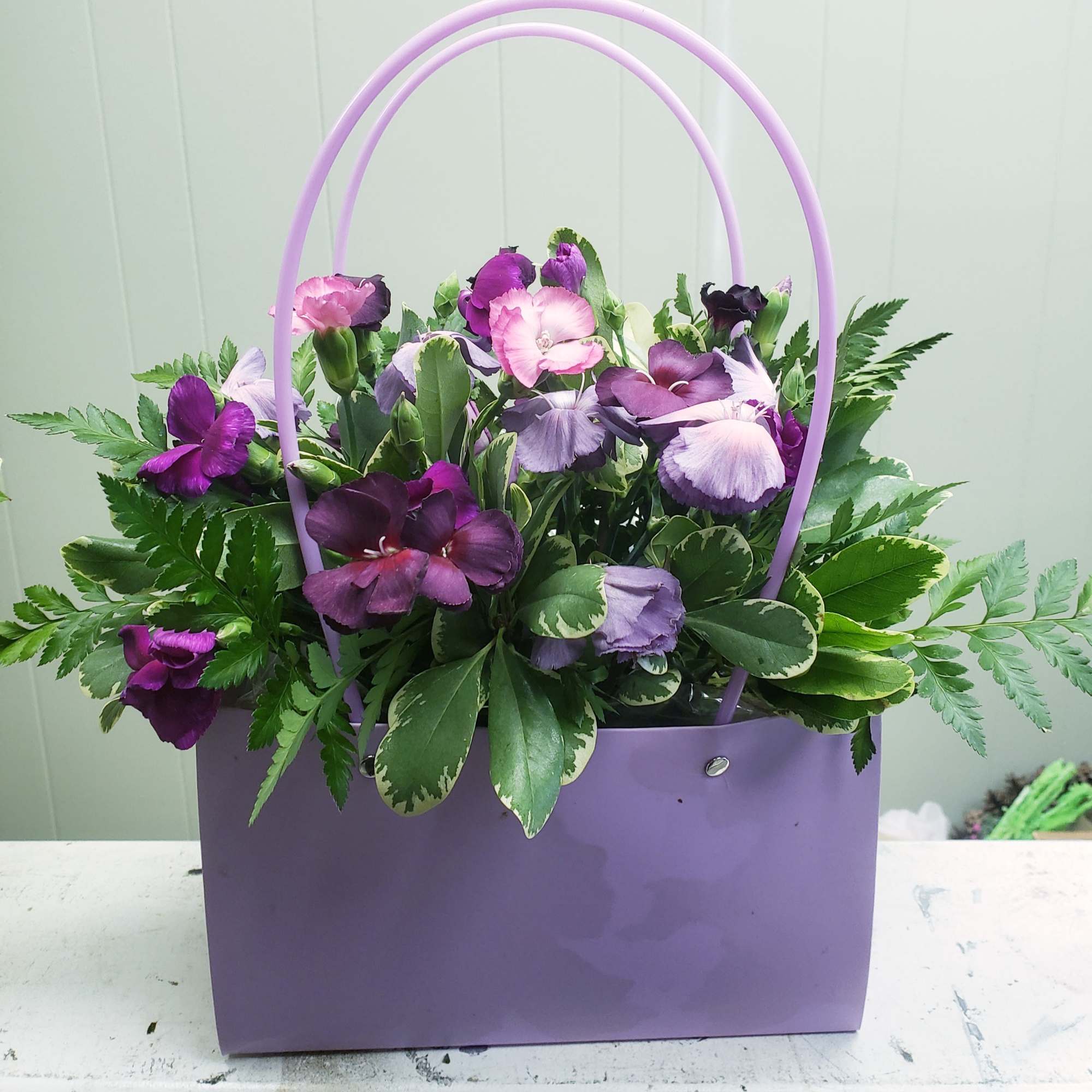 Purple and lavender flowers in a lavender handbag-style container with double handles