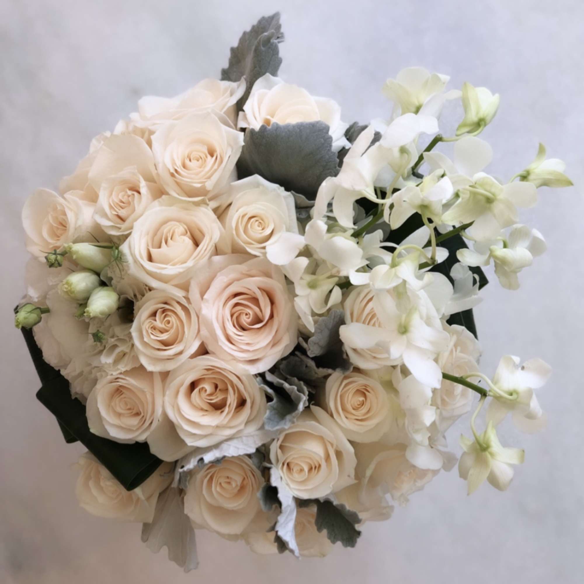 Bouquet of pale peach roses and white orchids with gray foliage