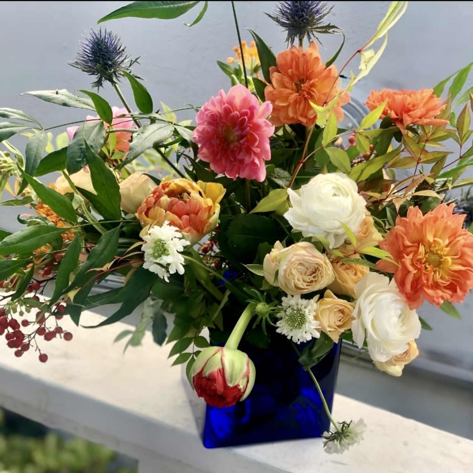 Asymmetrical arrangement of orange, pink, and cream flowers in a cobalt blue glass cube vase