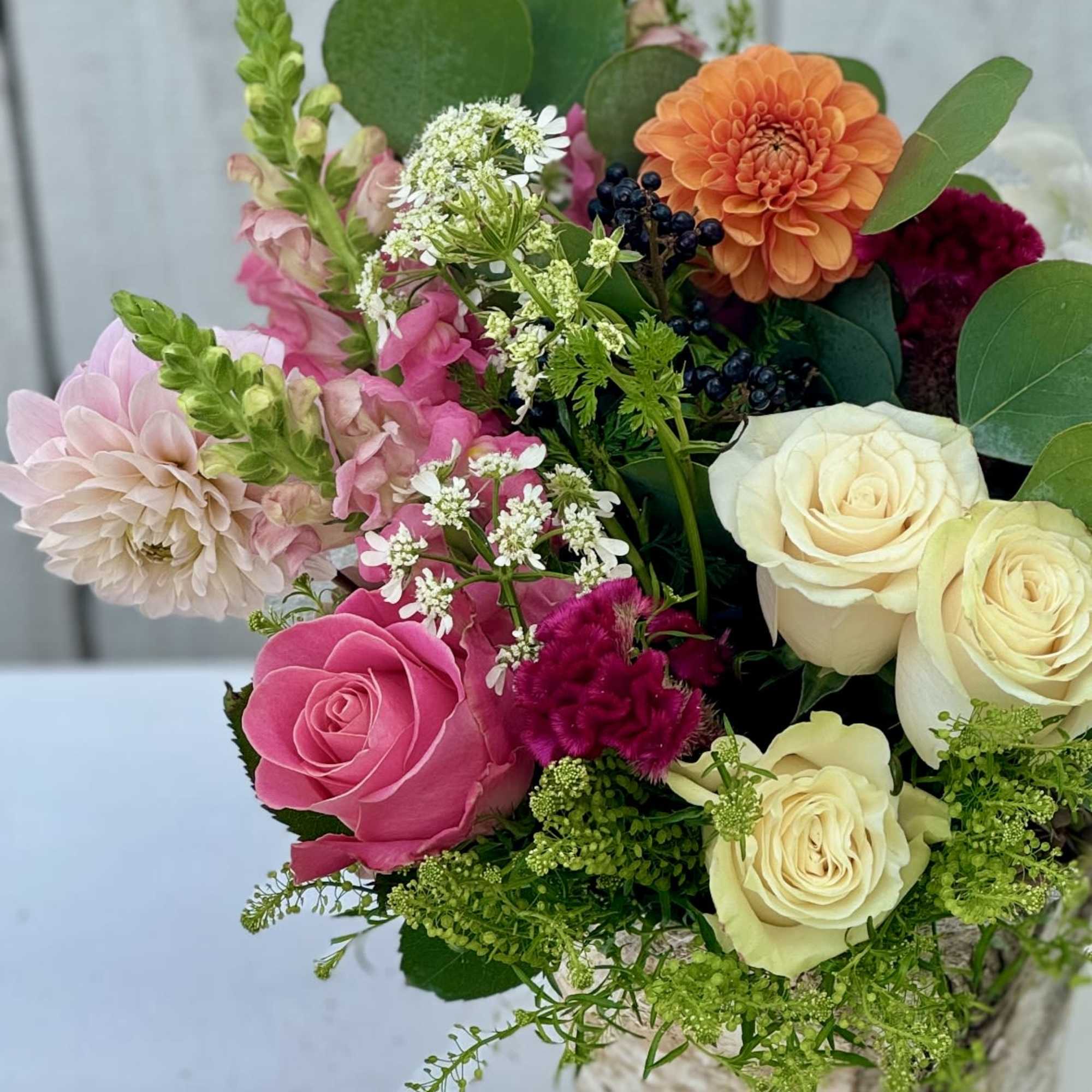 Mixed bouquet of roses, dahlias, and pink blooms in a rustic container