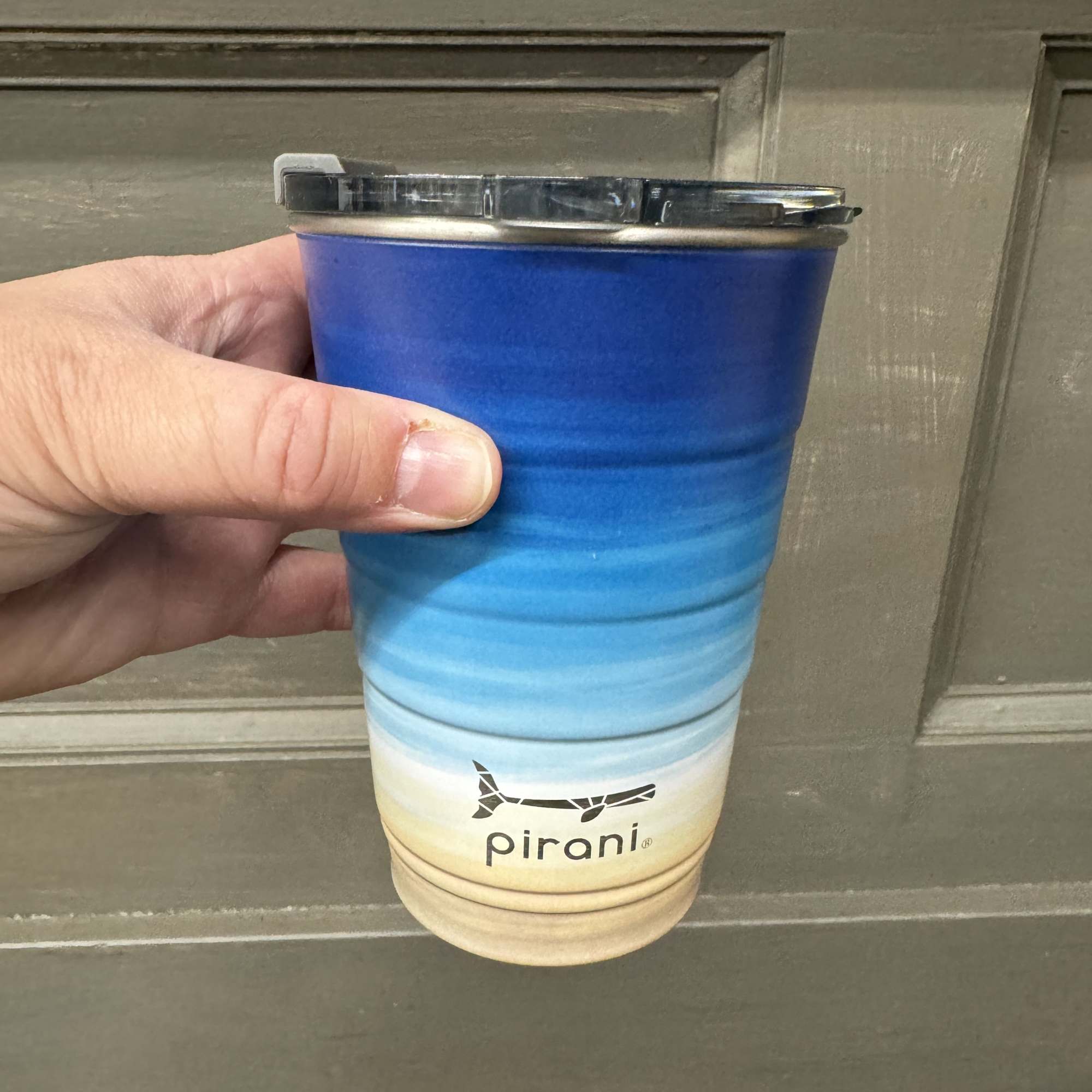 Hand holding a blue-to-beige insulated travel cup with a lid
