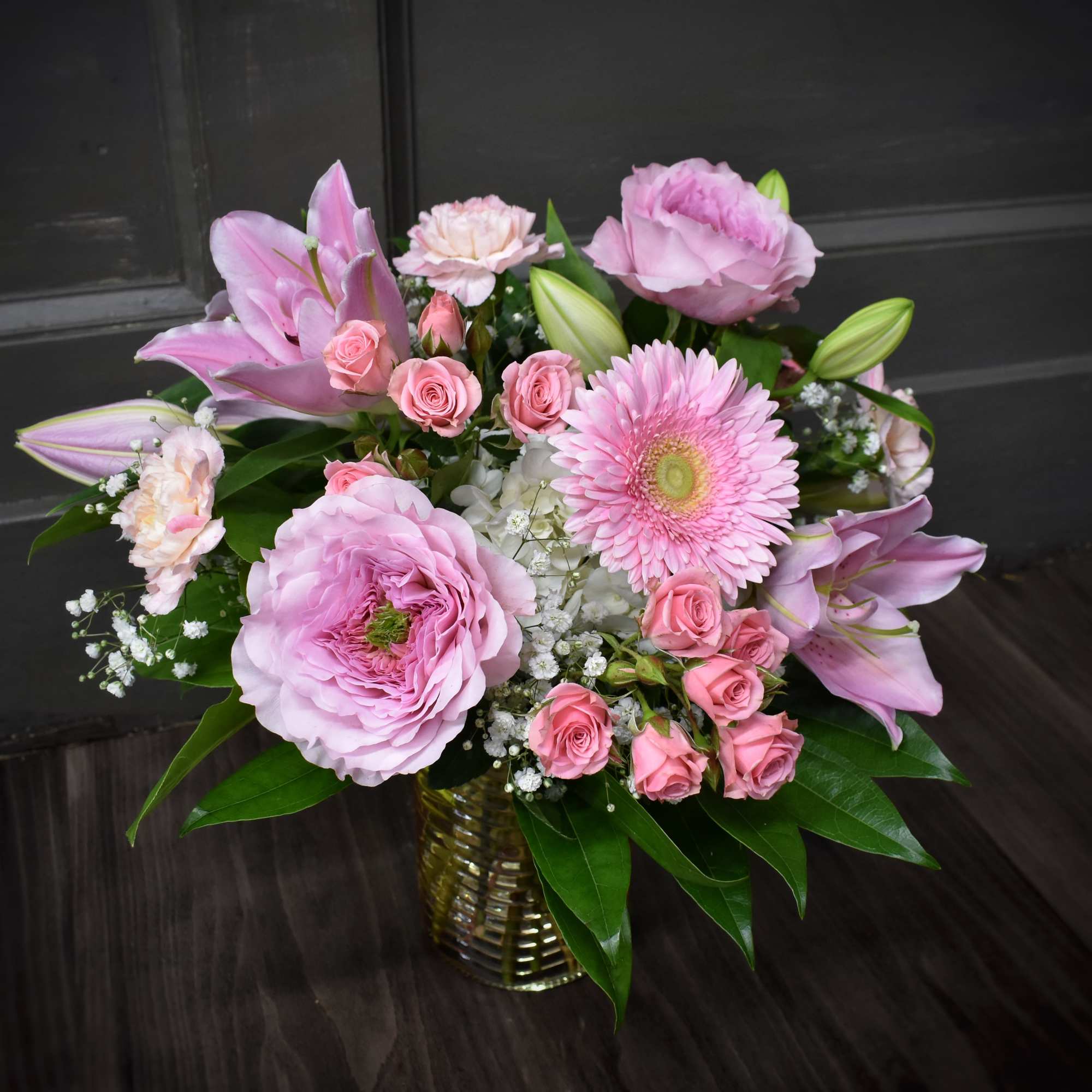 Pink mixed bouquet in a gold vase with lilies, roses, and a gerbera daisy