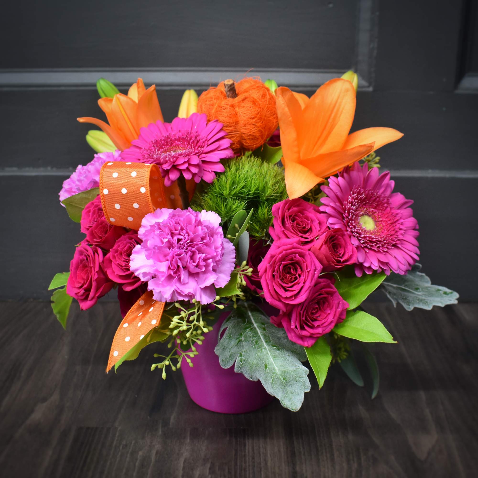 Bright bouquet of orange lilies, pink gerberas, and roses in a magenta vase