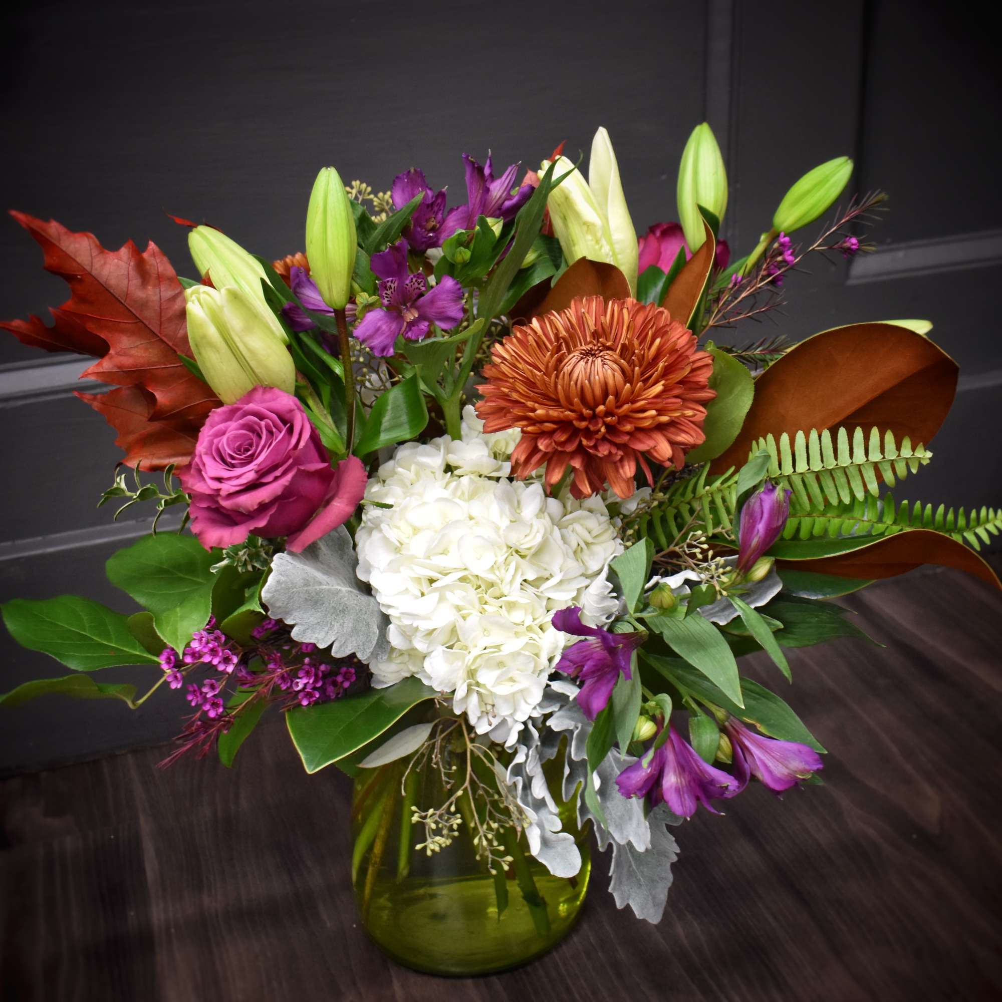 Mixed bouquet with white hydrangea, purple roses, lilies, and chrysanthemums in a green vase