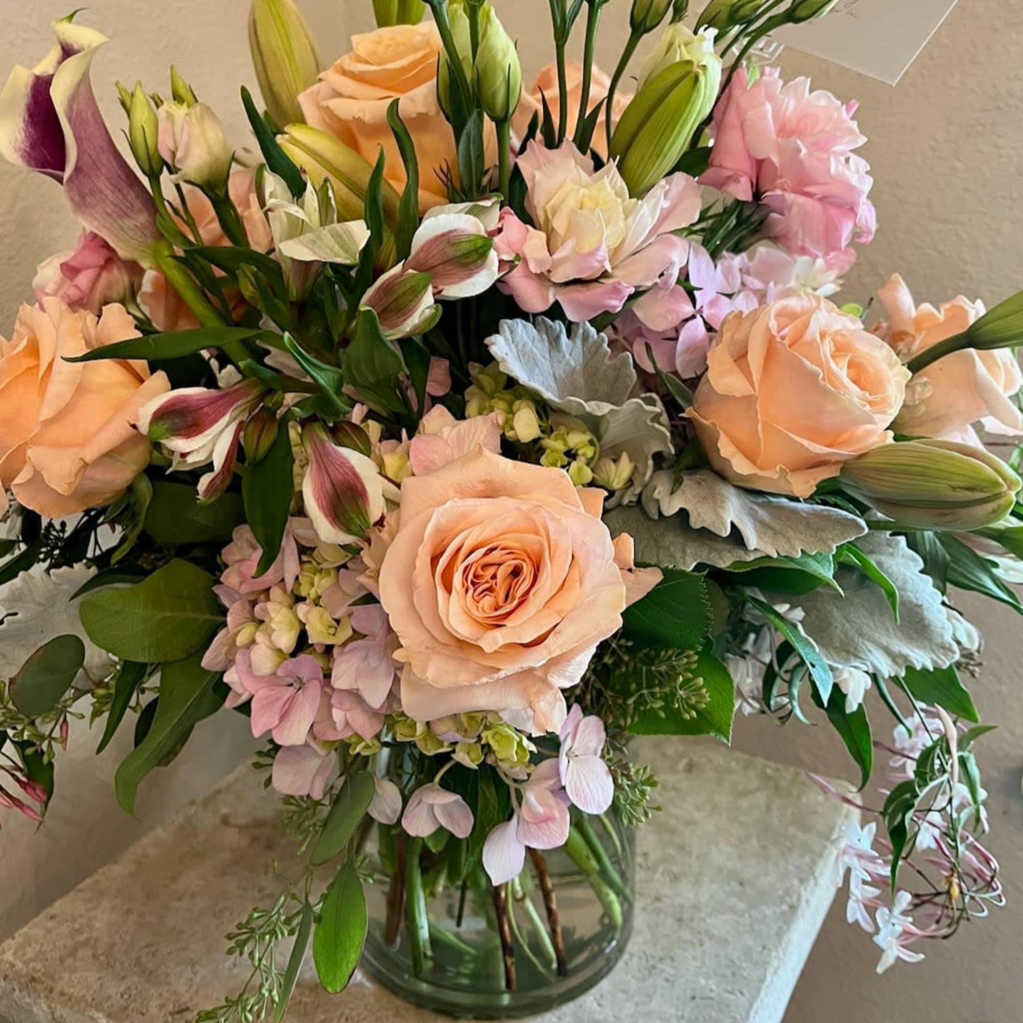 Bouquet of peach roses, pink blooms, and lilies in a glass vase