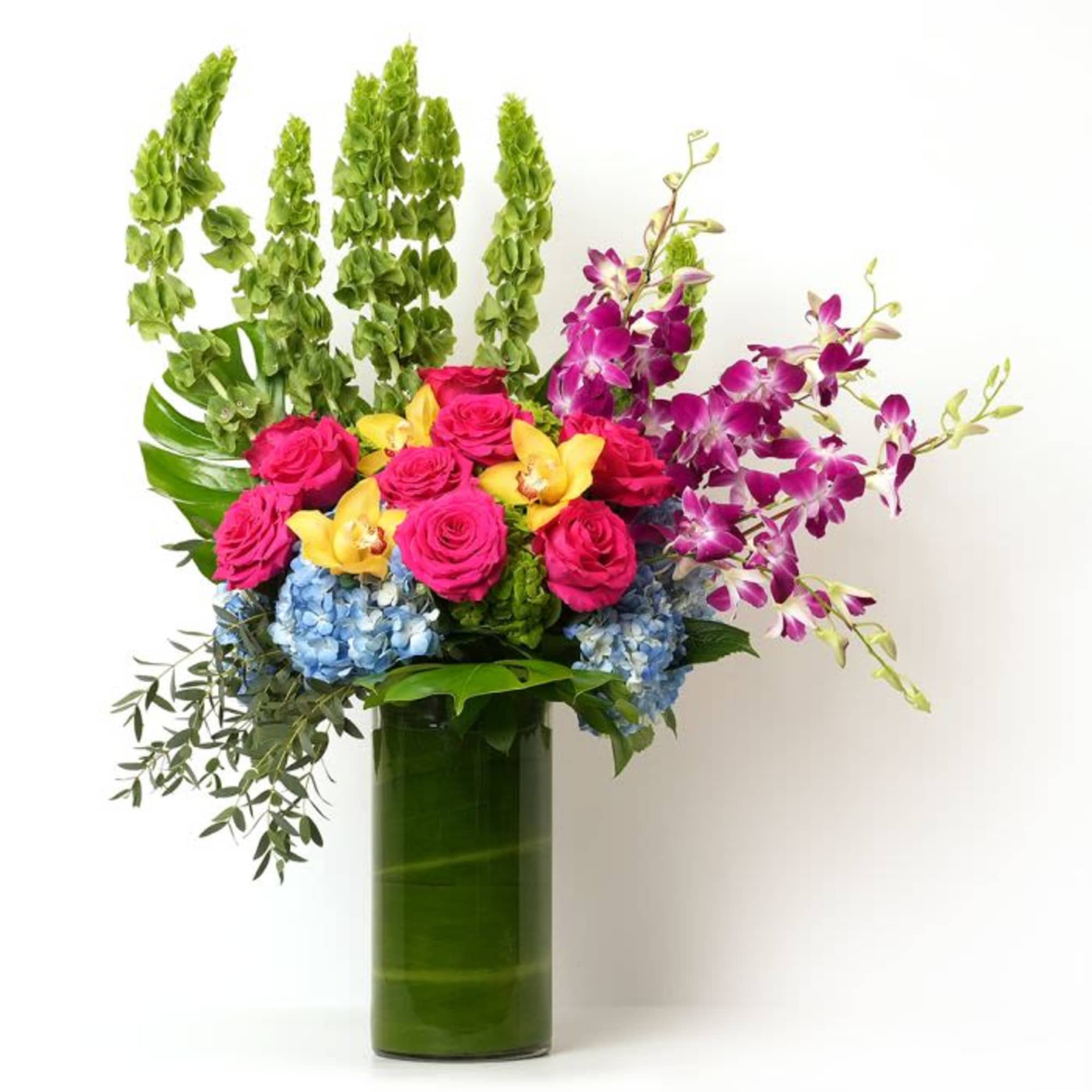 Tall arrangement of pink roses, orchids, and blue hydrangeas in a green-lined glass cylinder vase