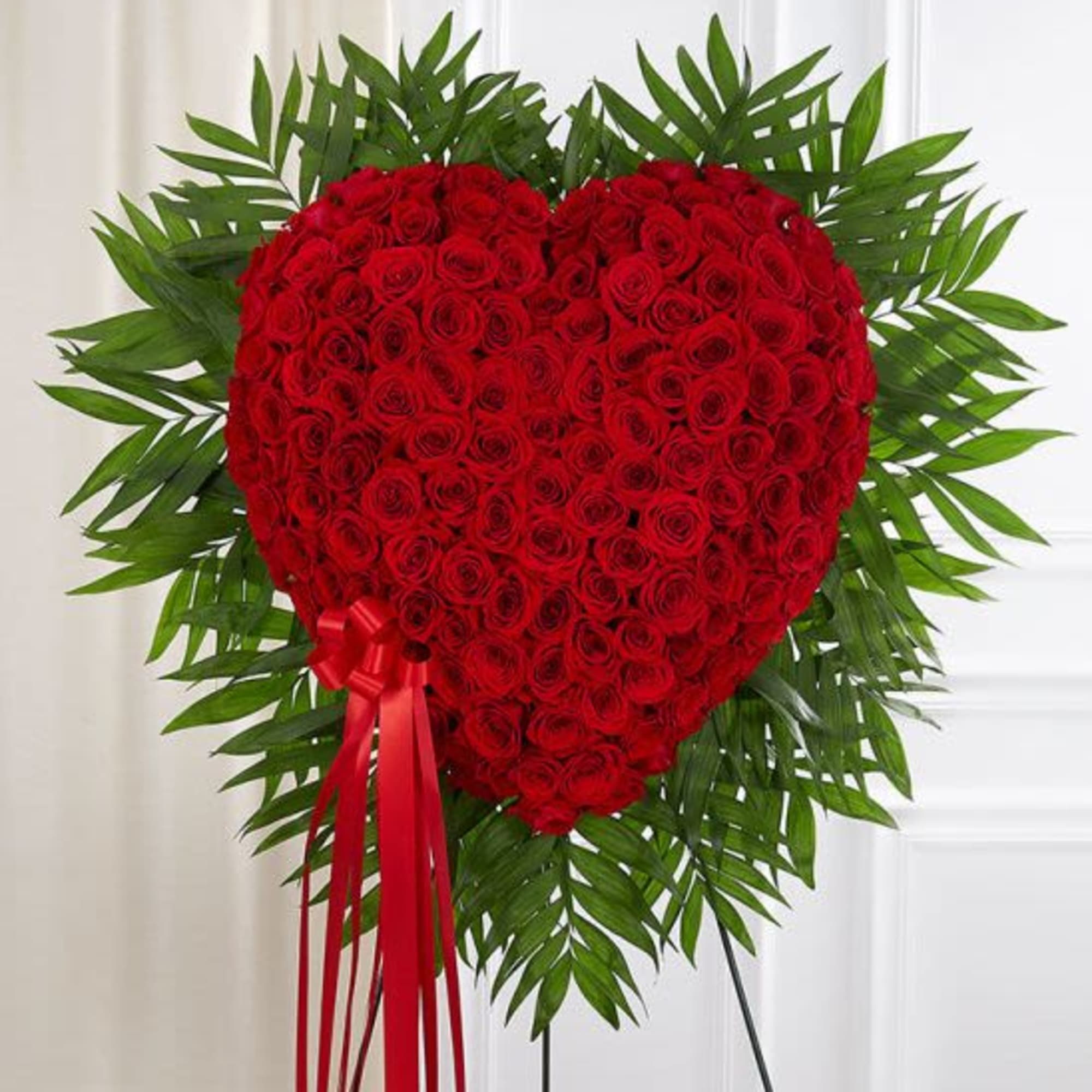 Tall heart-shaped arrangement of red roses with a red ribbon on a stand.