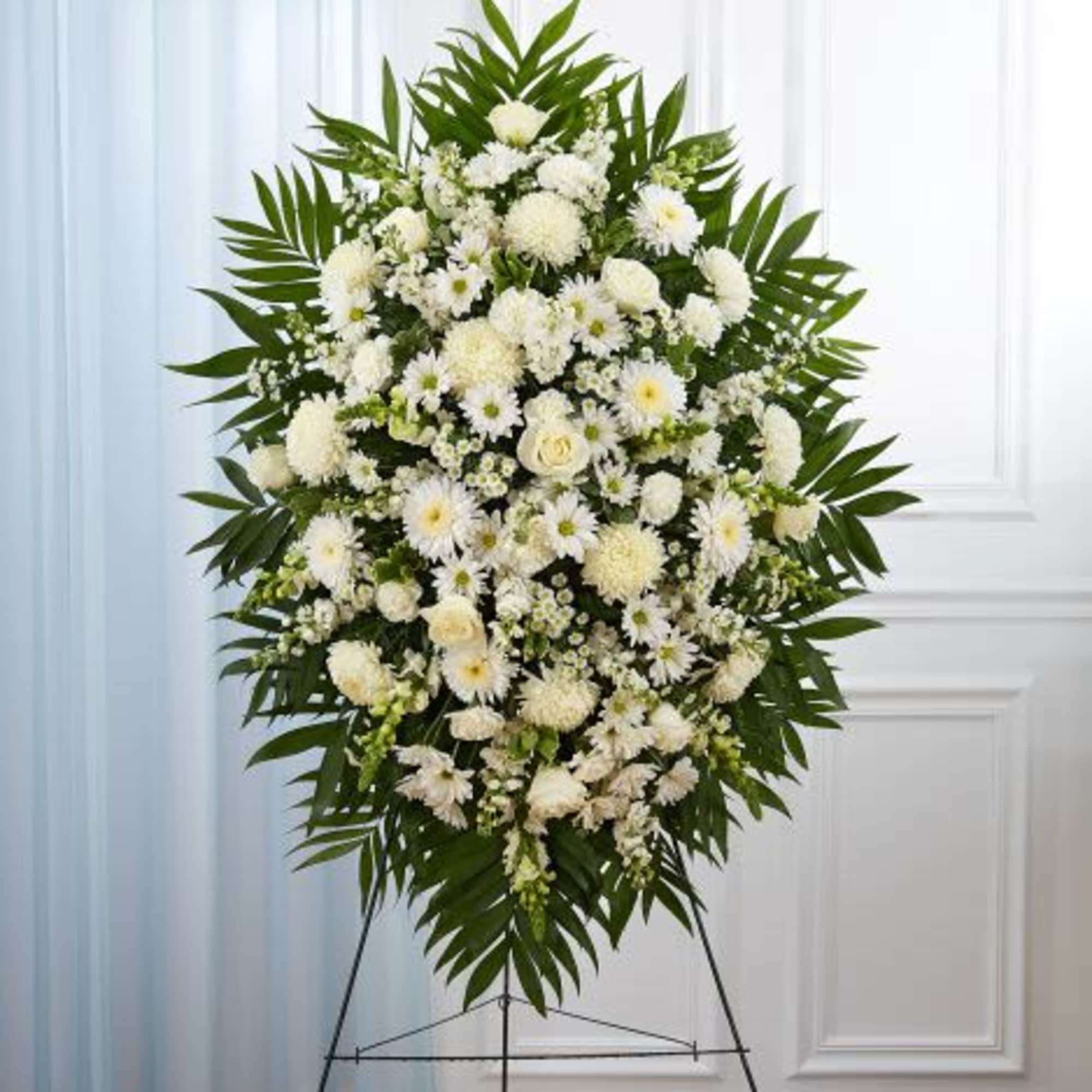 Tall white standing spray of roses, daisies, and mums with bold greenery on a metal easel.