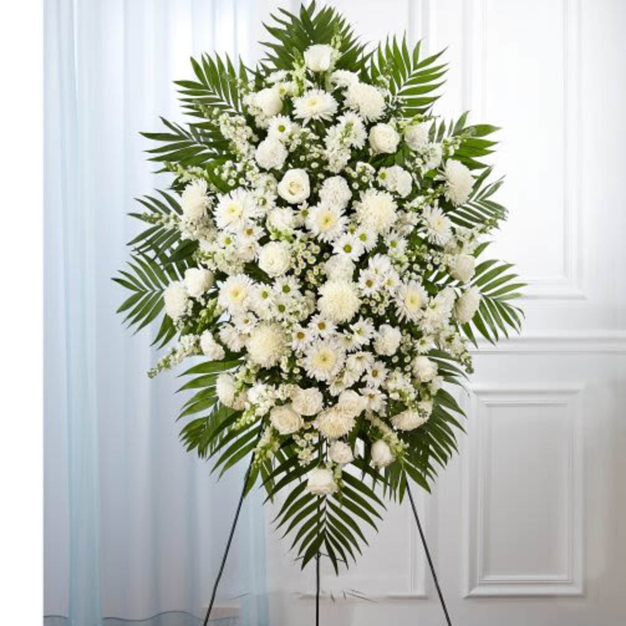 Tall standing spray of white roses, mums, and daisies on an easel with palm fronds.
