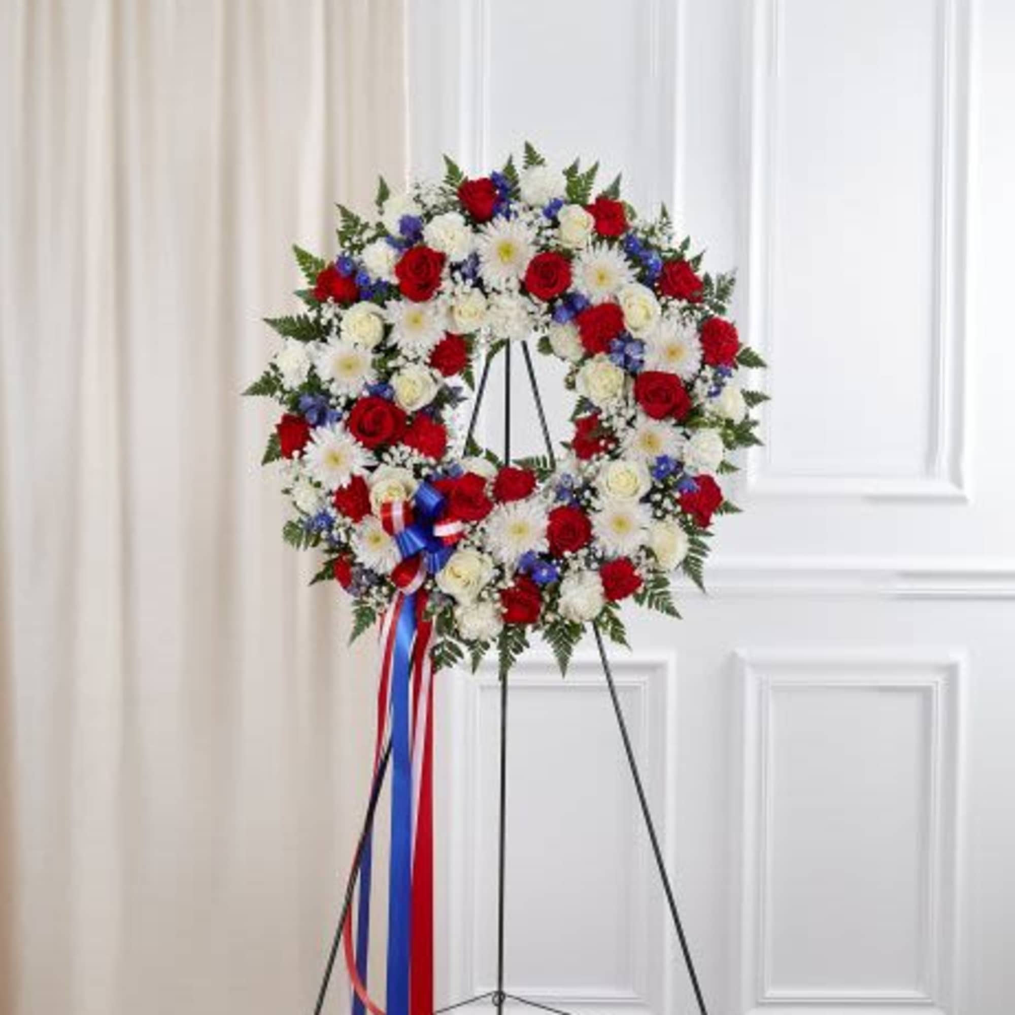 Patriotic red, white, and blue floral wreath on a metal easel with long ribbon streamers