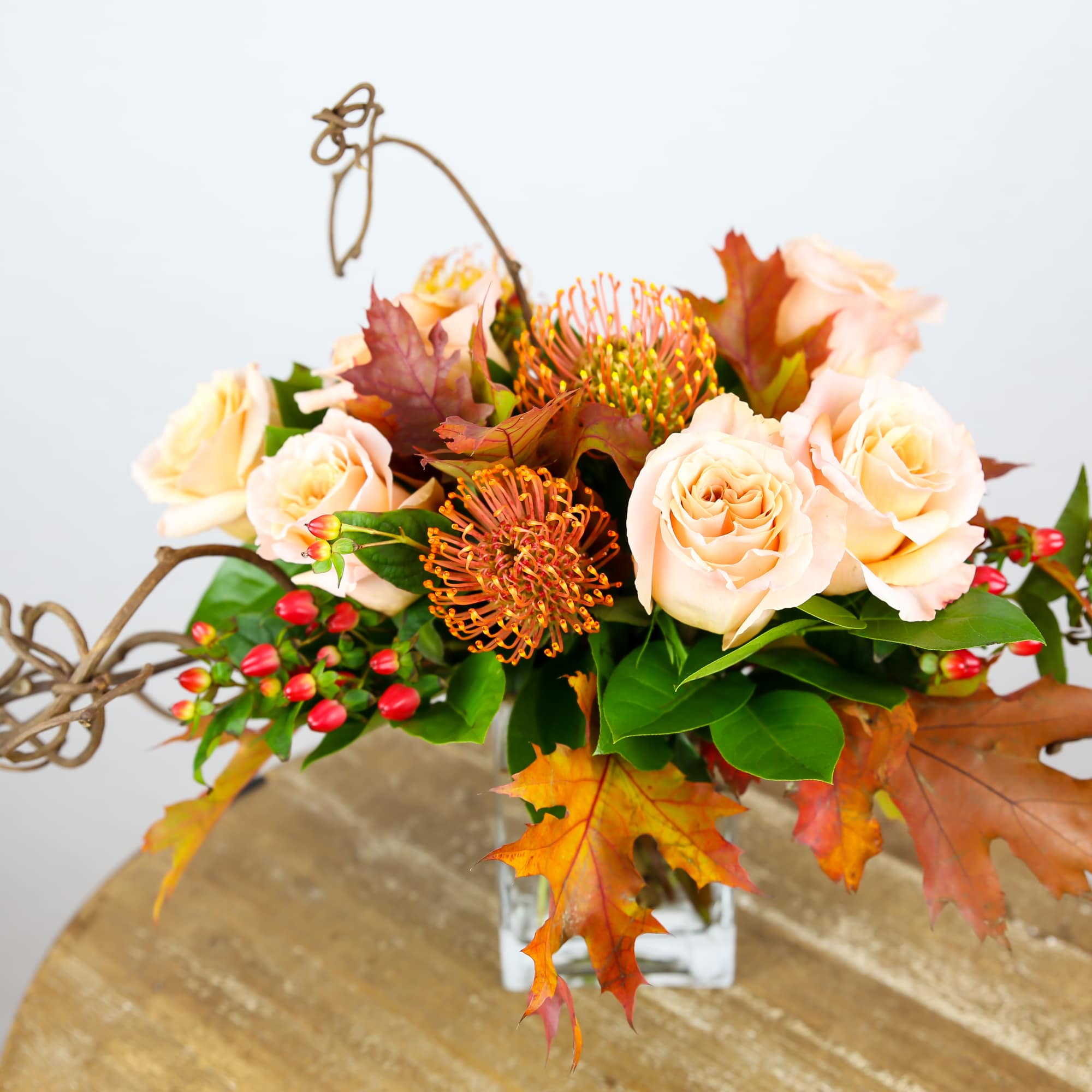 Peach roses and orange blooms in a glass vase with autumn leaves