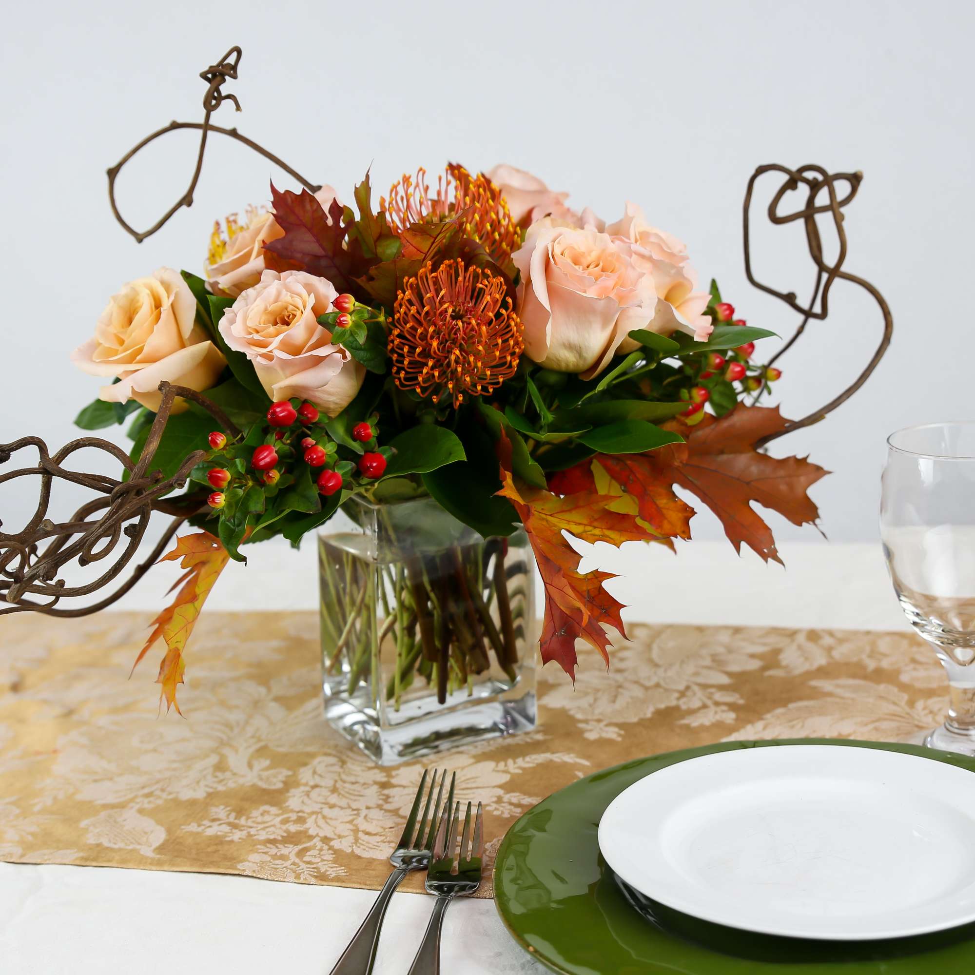 Peach roses in a glass vase with autumn leaves and wire accents on a table setting