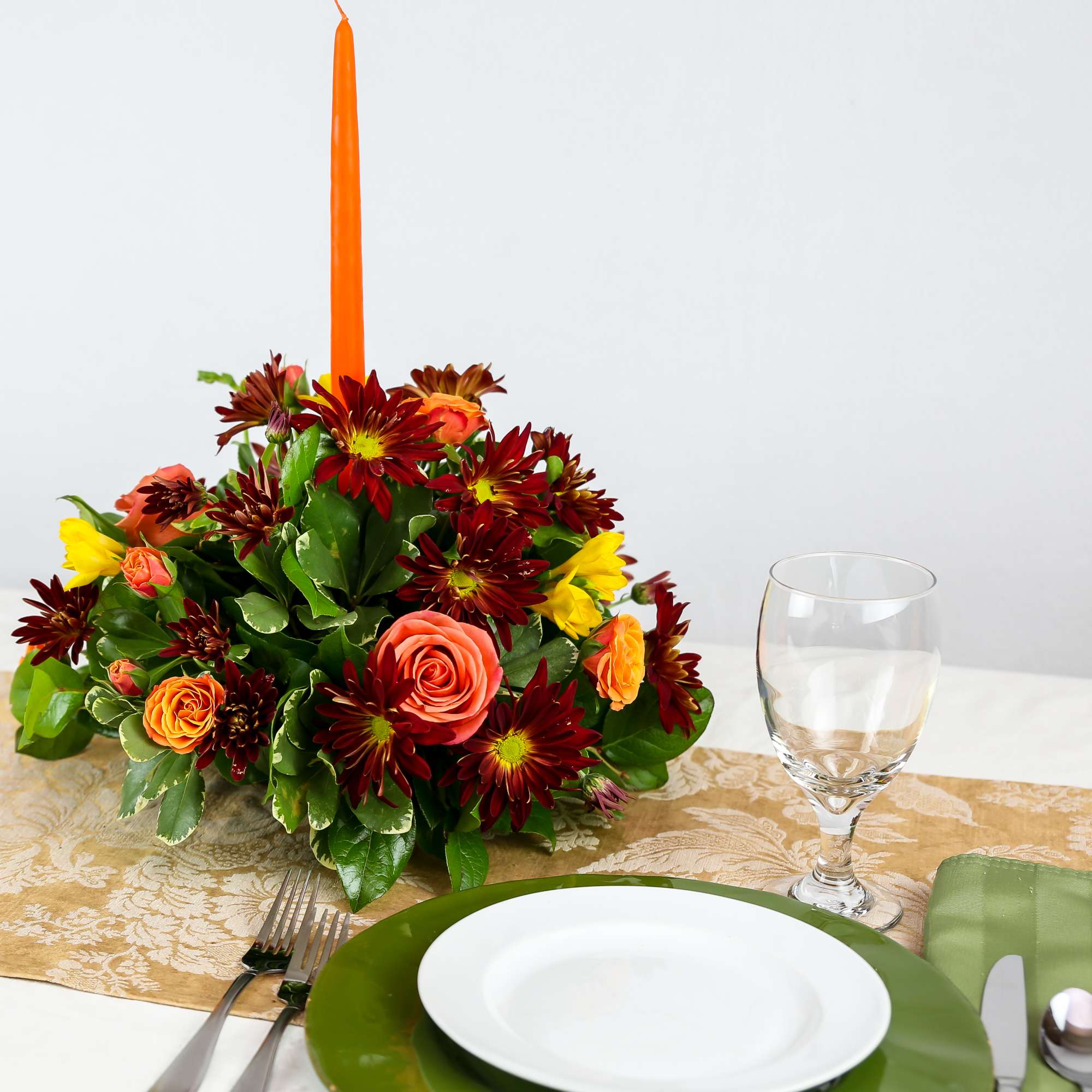 Autumn floral centerpiece with a tall orange candle on a table setting
