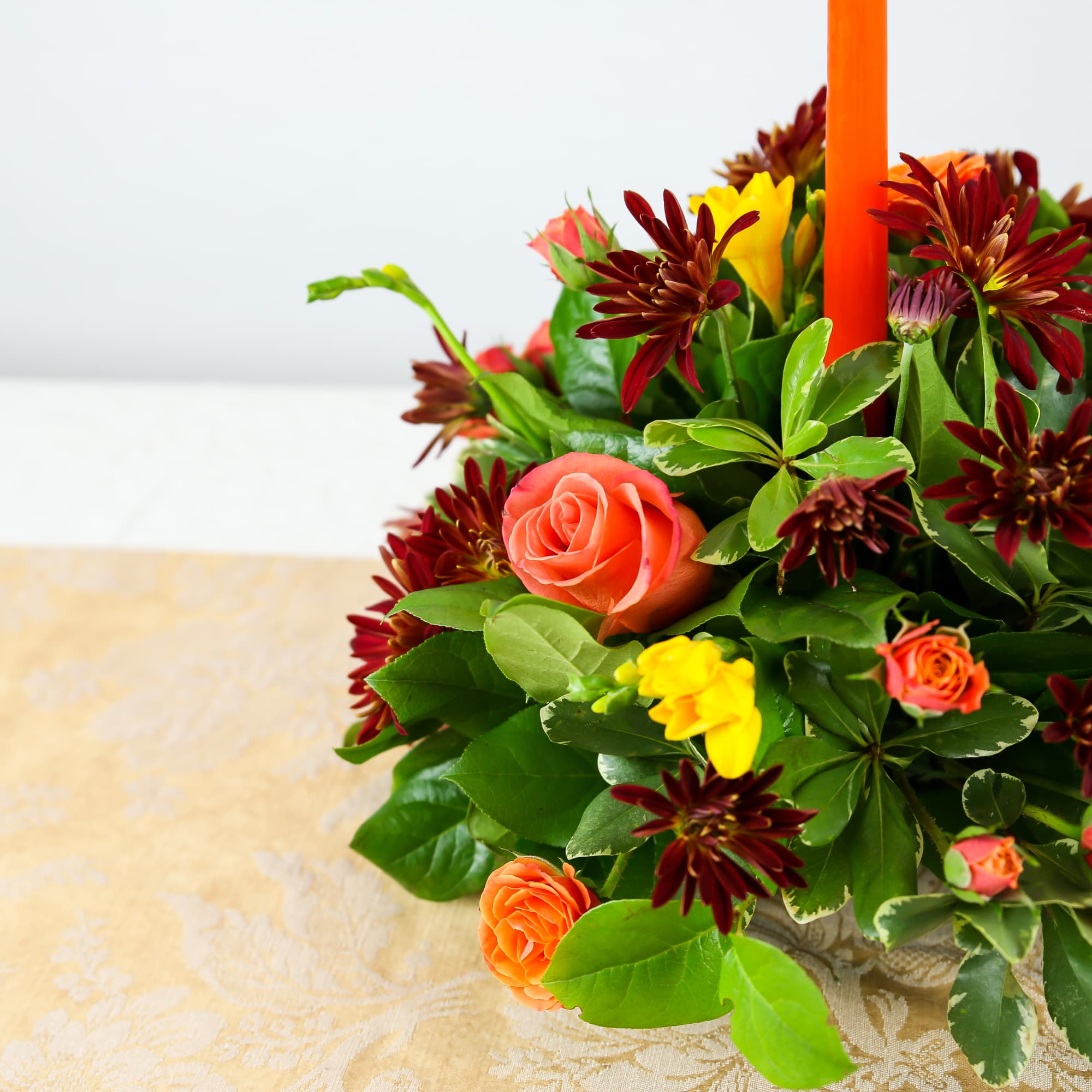 Orange and burgundy floral arrangement with a tall orange candle