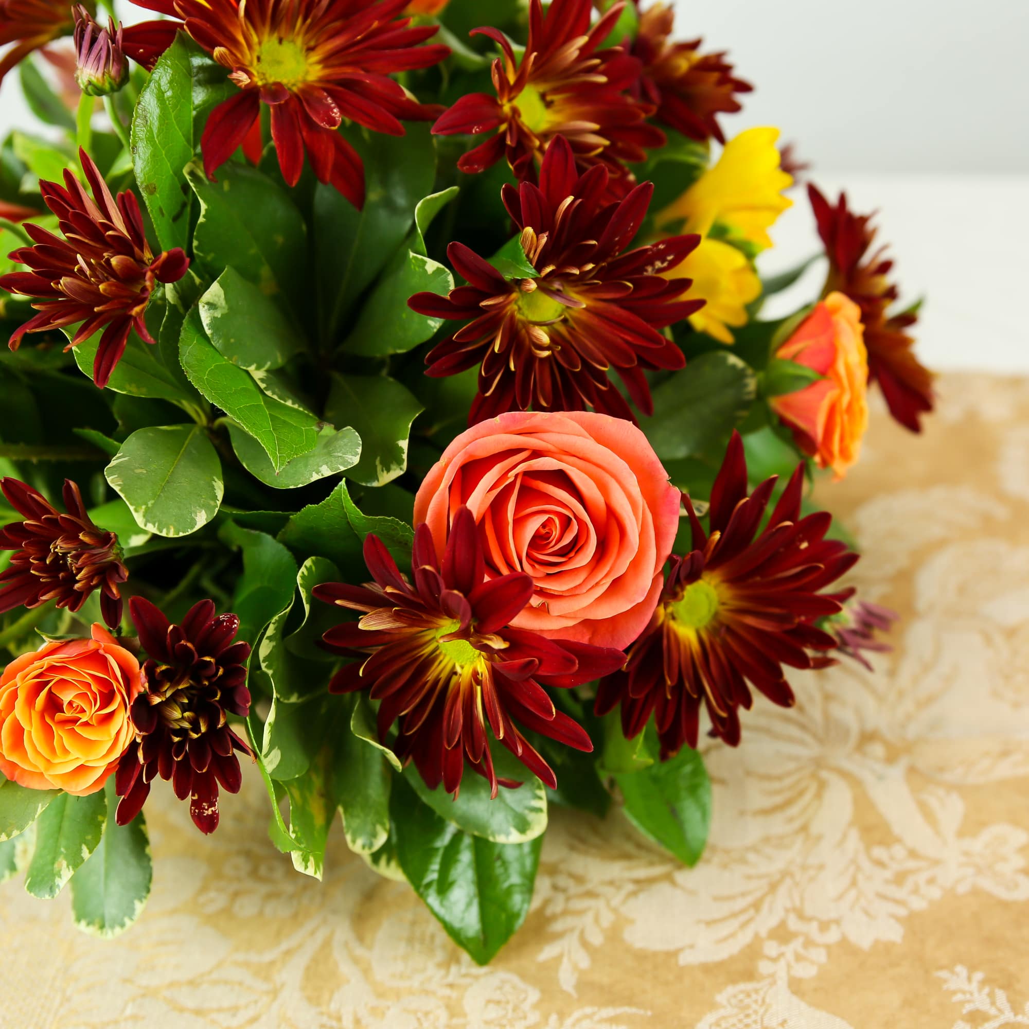 Orange roses and burgundy daisies in a low floral arrangement