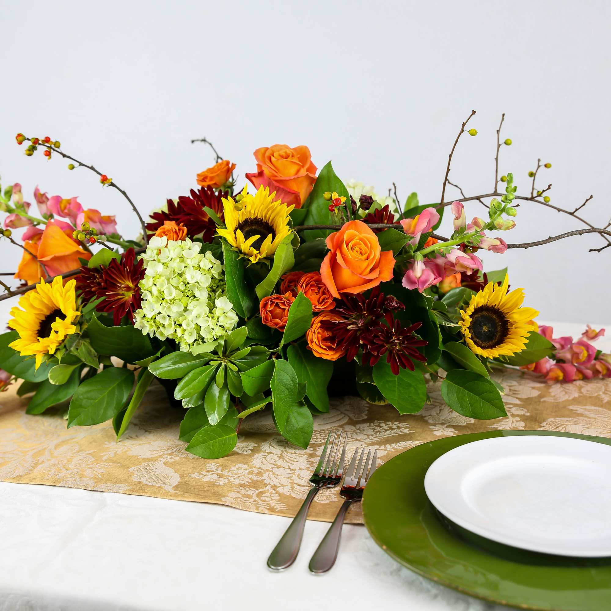 Low floral centerpiece with sunflowers, orange roses, and burgundy blooms on a table