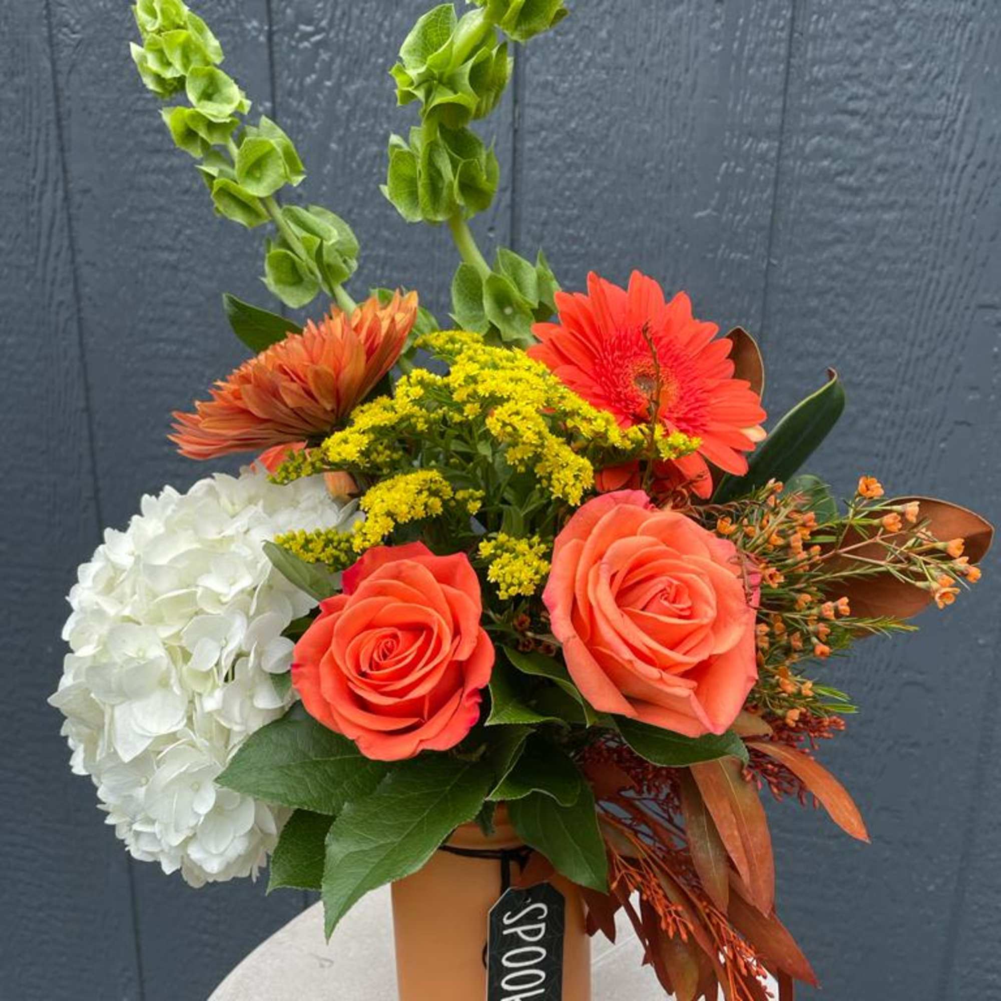 Orange and white floral arrangement in a vase with tall green spikes
