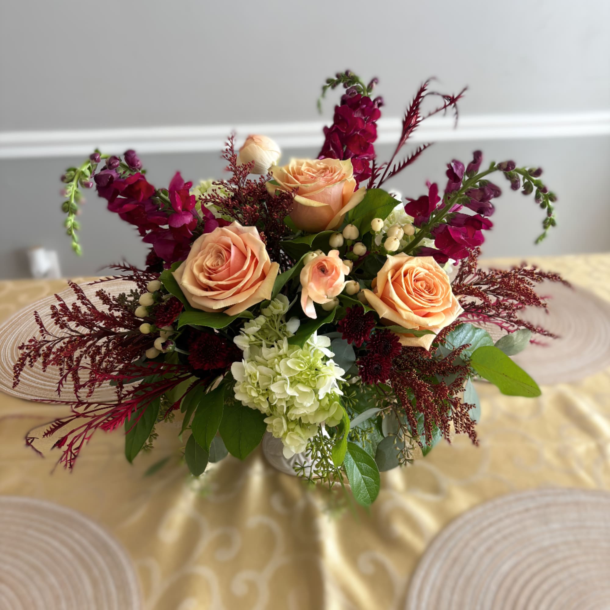 Peach roses and burgundy flowers arranged in a low vase
