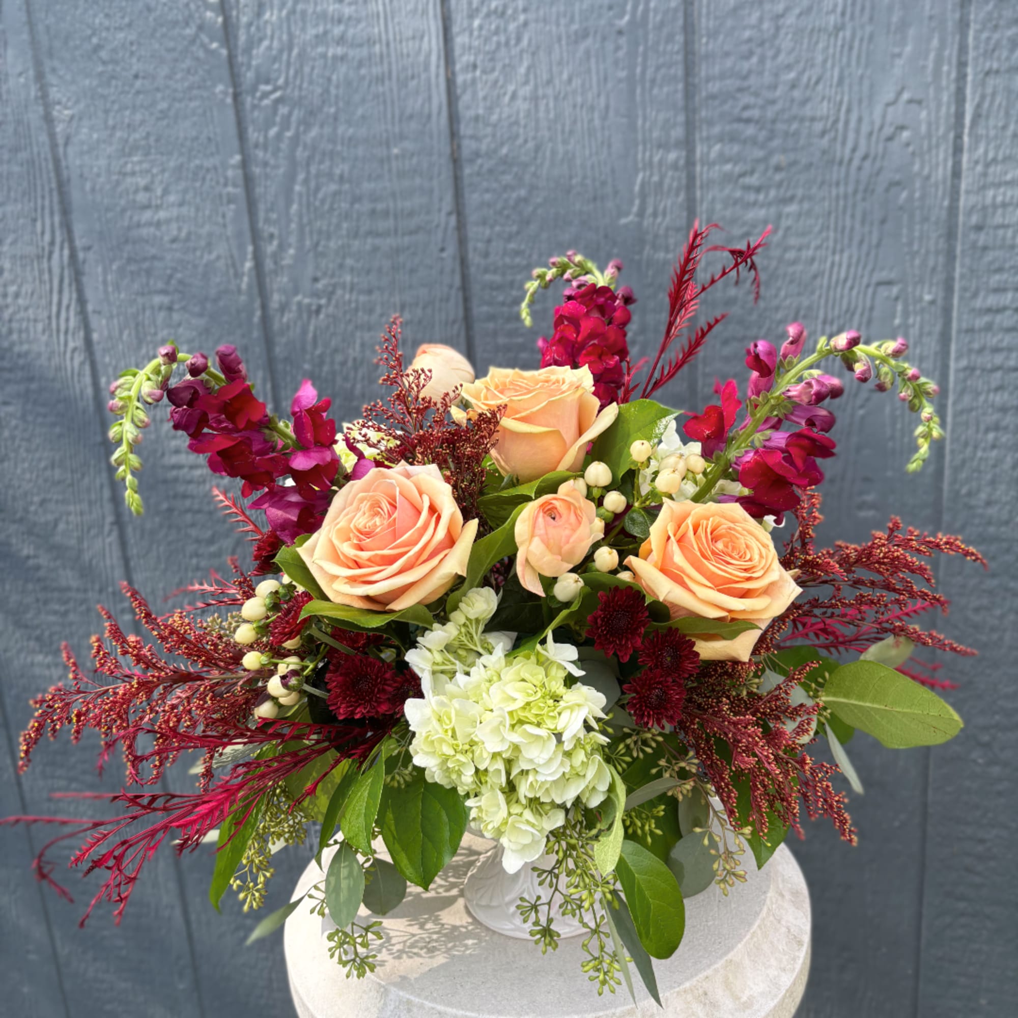 Peach roses and burgundy flowers in a white vase