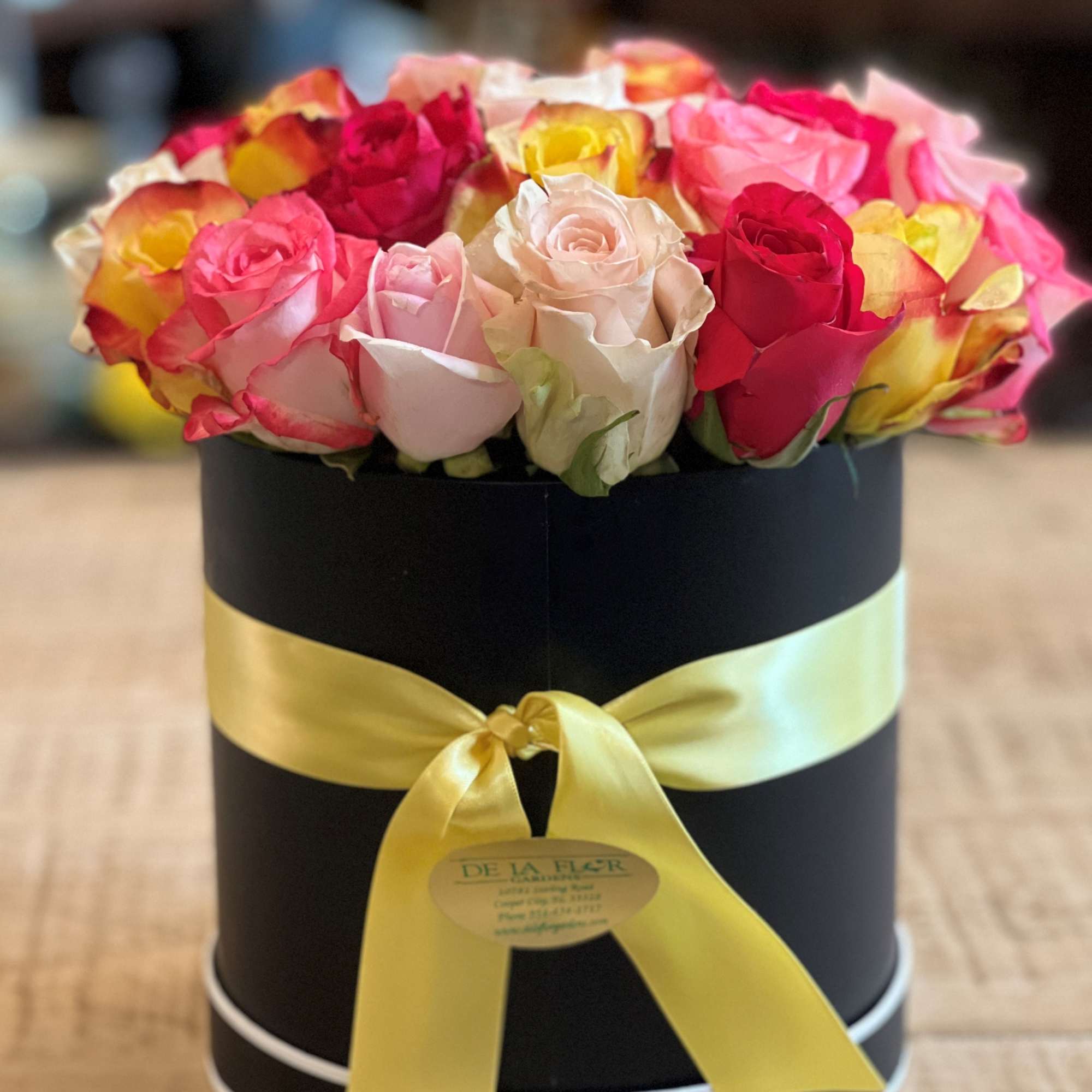Mixed roses in a black round box with a yellow ribbon
