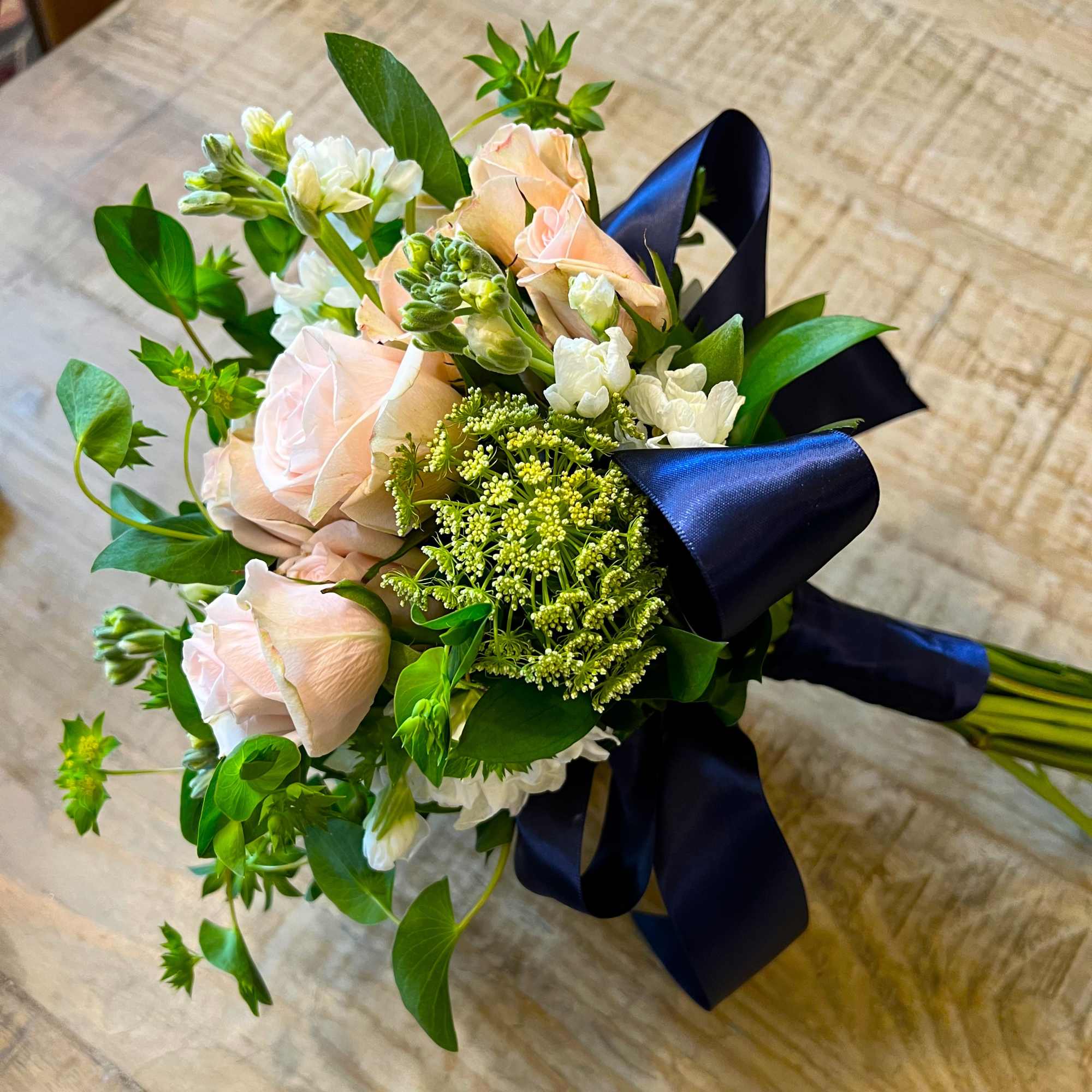 Bouquet of pale pink roses and white flowers tied with a dark blue ribbon