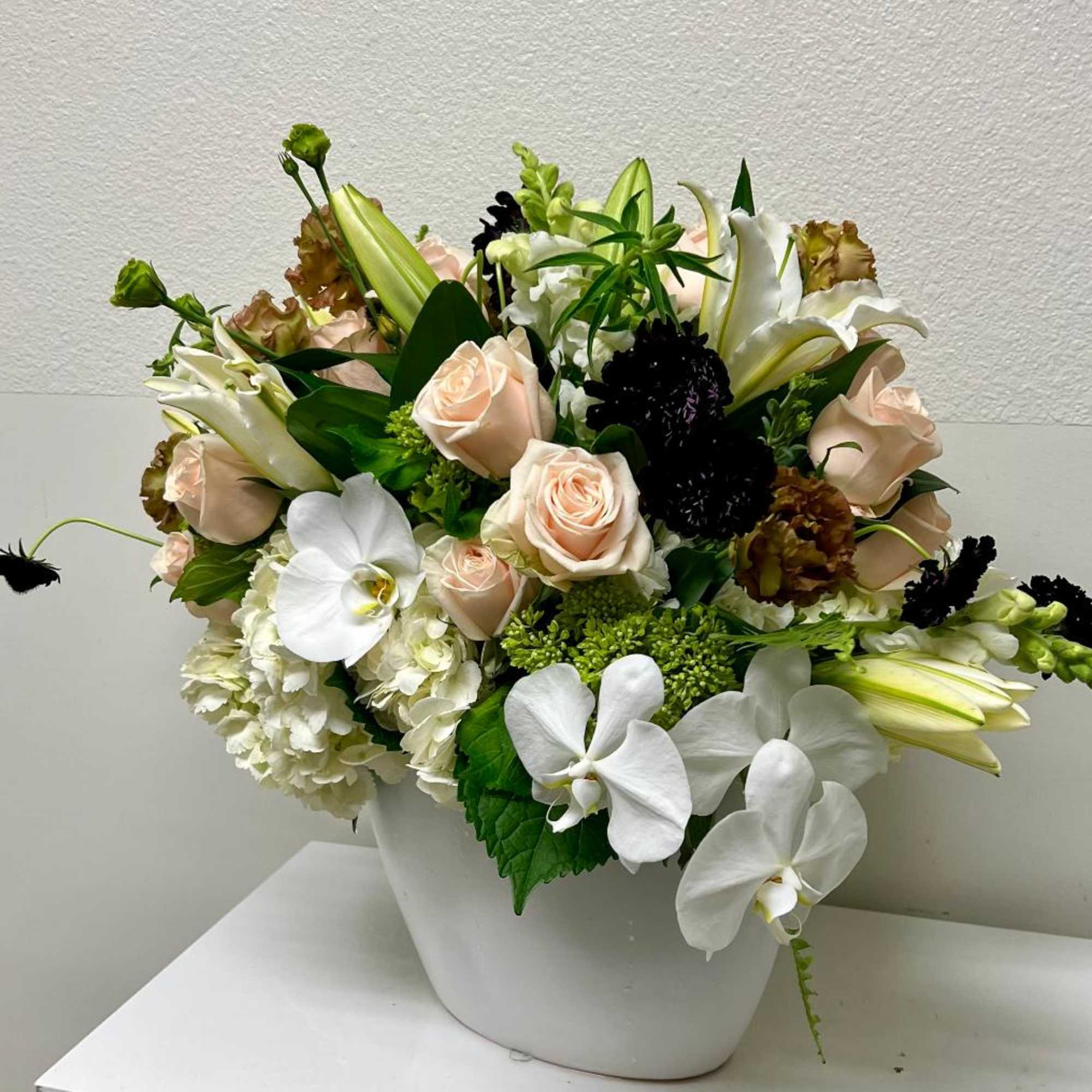 White vase arrangement with pale roses, white orchids, lilies, and hydrangeas