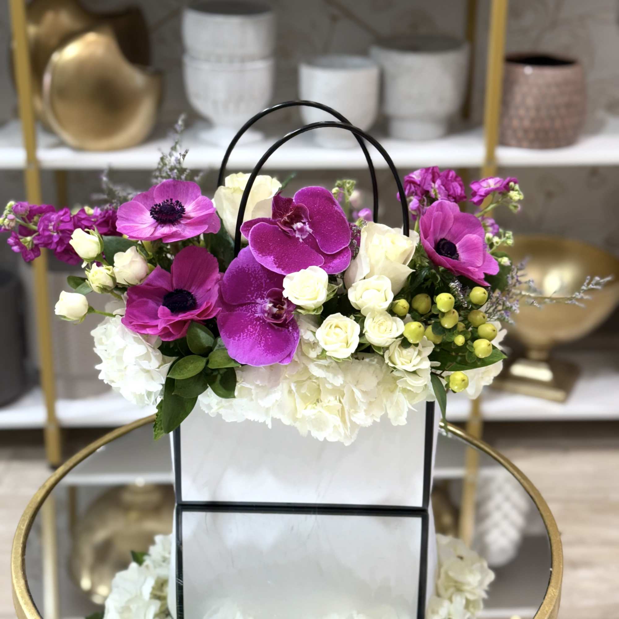 Pink and white flowers arranged in a white gift bag with black handles.