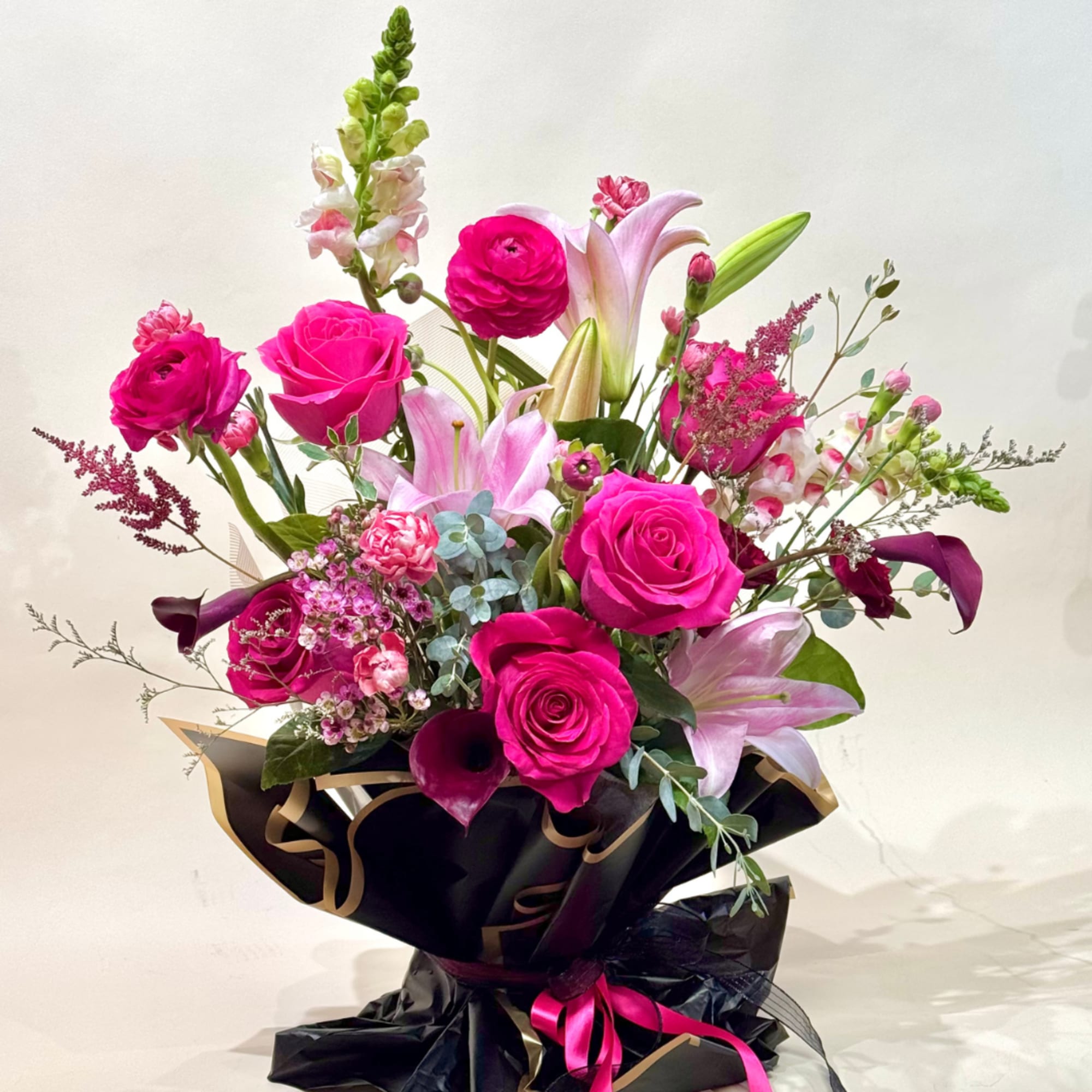 Bouquet of pink roses and lilies wrapped in black paper with a ribbon