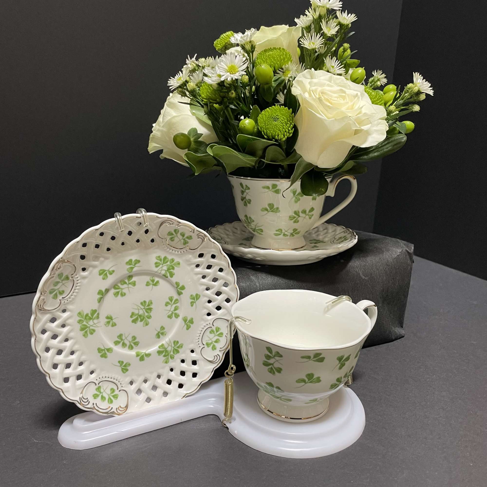 White roses and green button mums in a shamrock teacup arrangement
